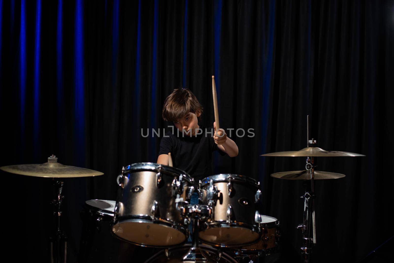 The boy learns to play the drums in the studio on a black background. Music school student by mrwed54