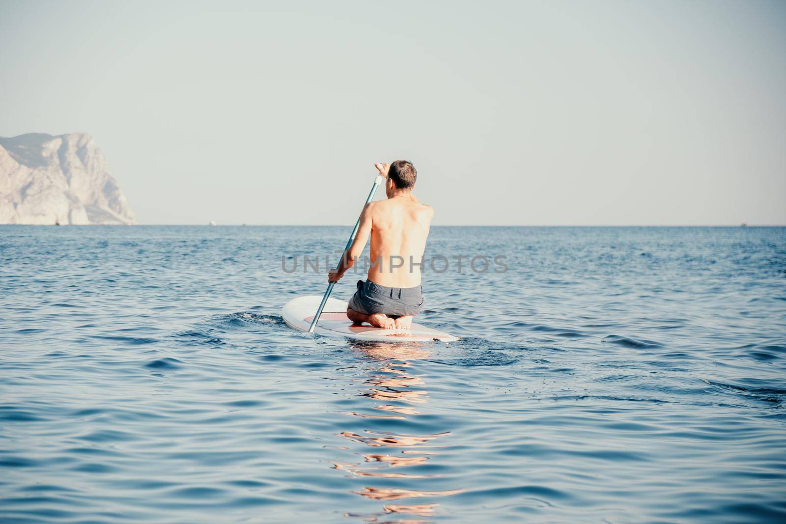 Side view foto of a man swiming and relaxing on the sup board. Sportive man in the sea on the Stand Up Paddle Board SUP. The concept of an active and healthy life in harmony with nature. by panophotograph