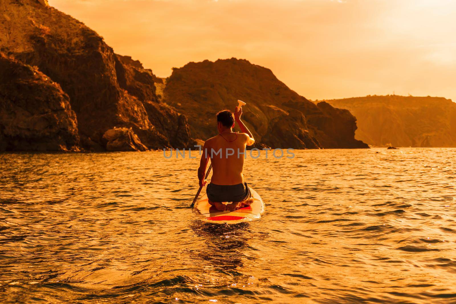 Side view foto of a man swiming and relaxing on the sup board. Sportive man in the sea on the Stand Up Paddle Board SUP. The concept of an active and healthy life in harmony with nature. by panophotograph