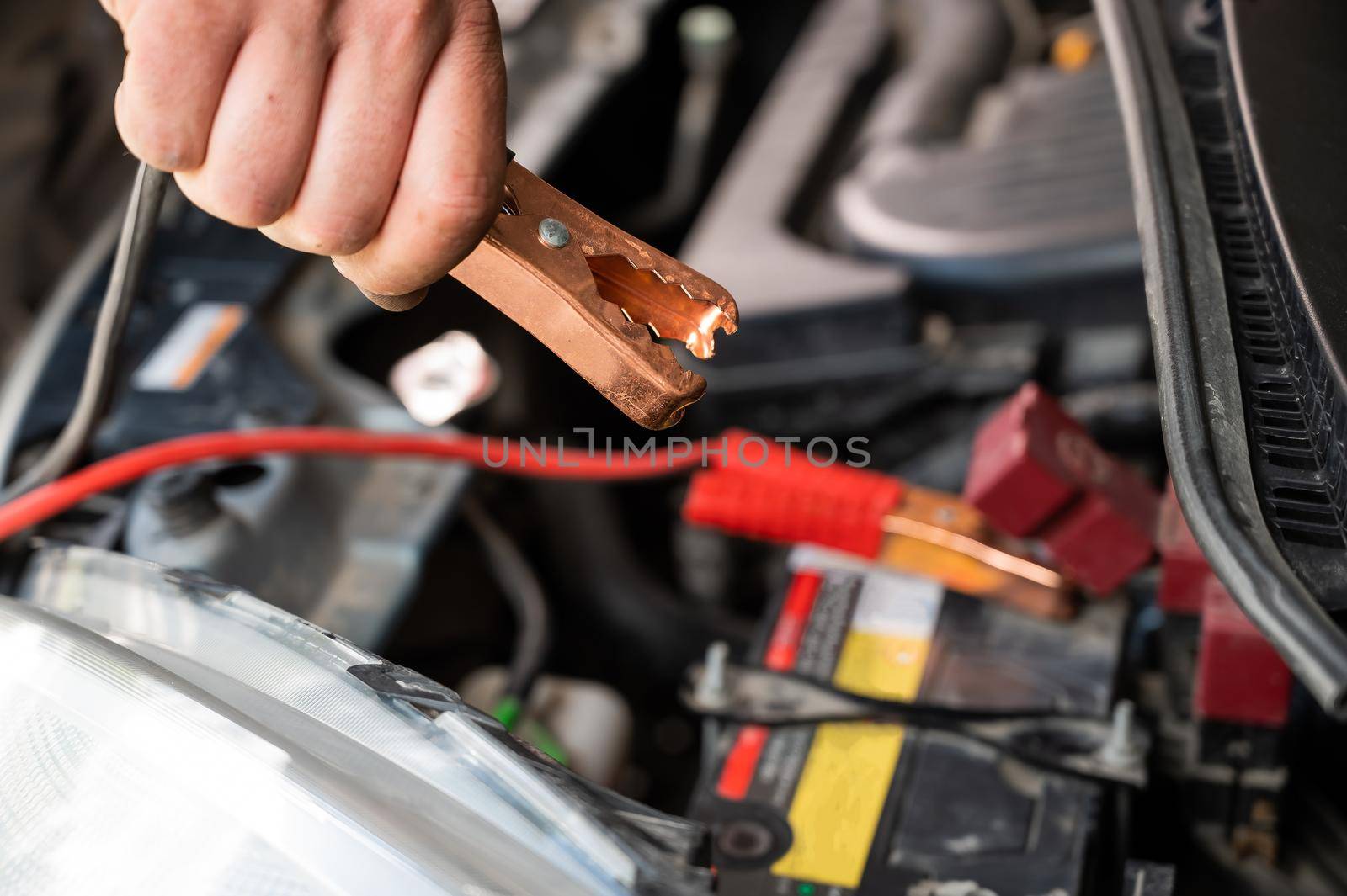 The mechanic connects the clamps to the discharged car battery