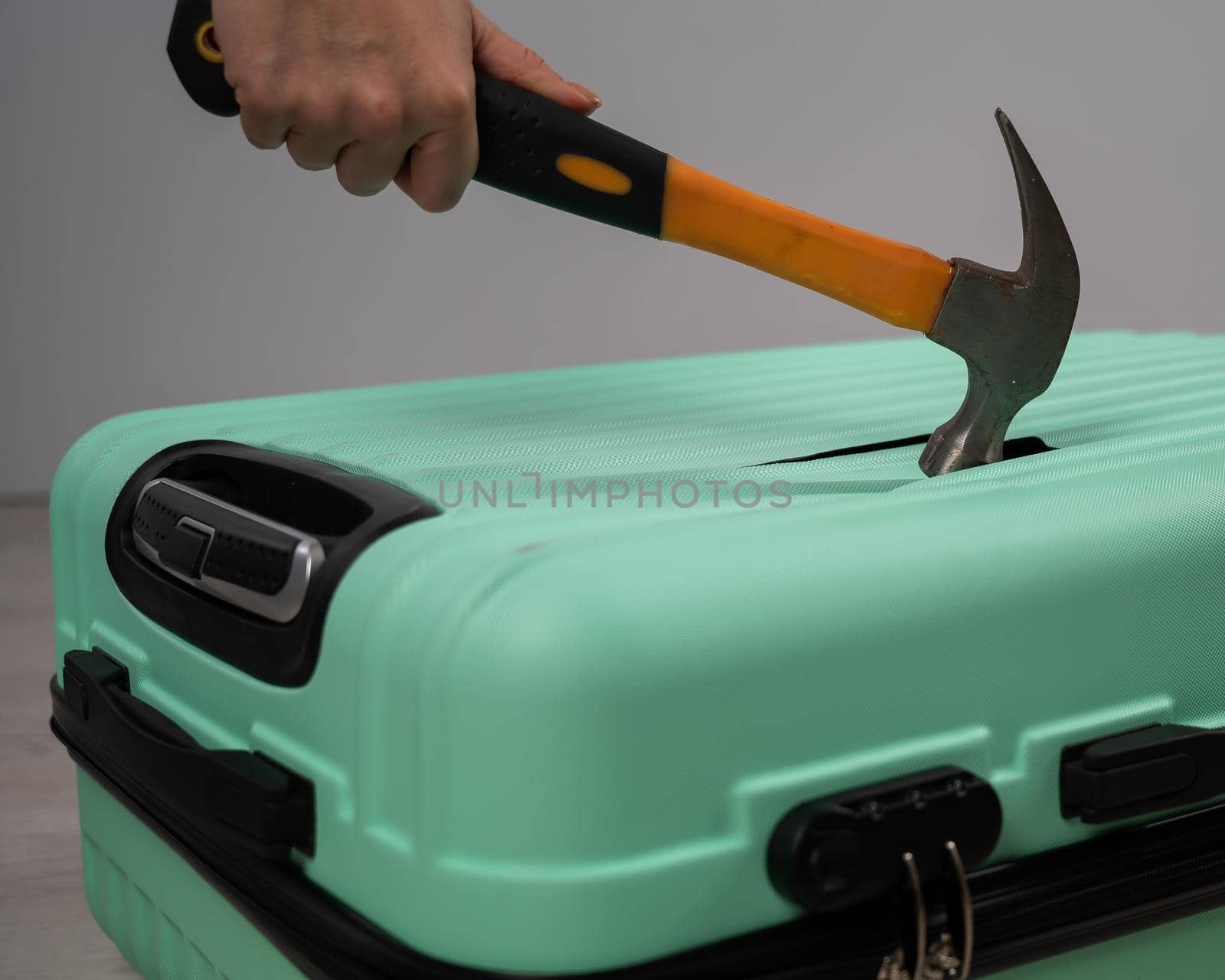 A woman hits a suitcase with a hammer on a white background