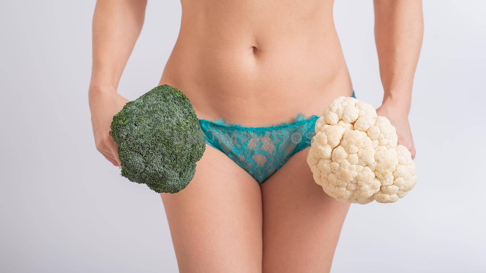 A faceless woman in panties holds cauliflower and broccoli on a white background. Food habits. by mrwed54