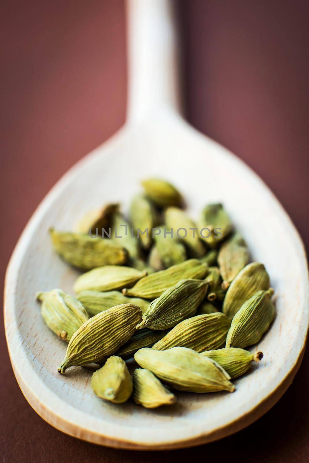 Whole cardamom in wooden spoon on brown background