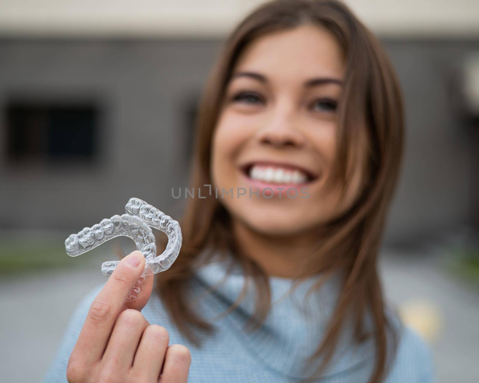 Caucasian woman with white smile holding transparent removable retainer. Bite correction device