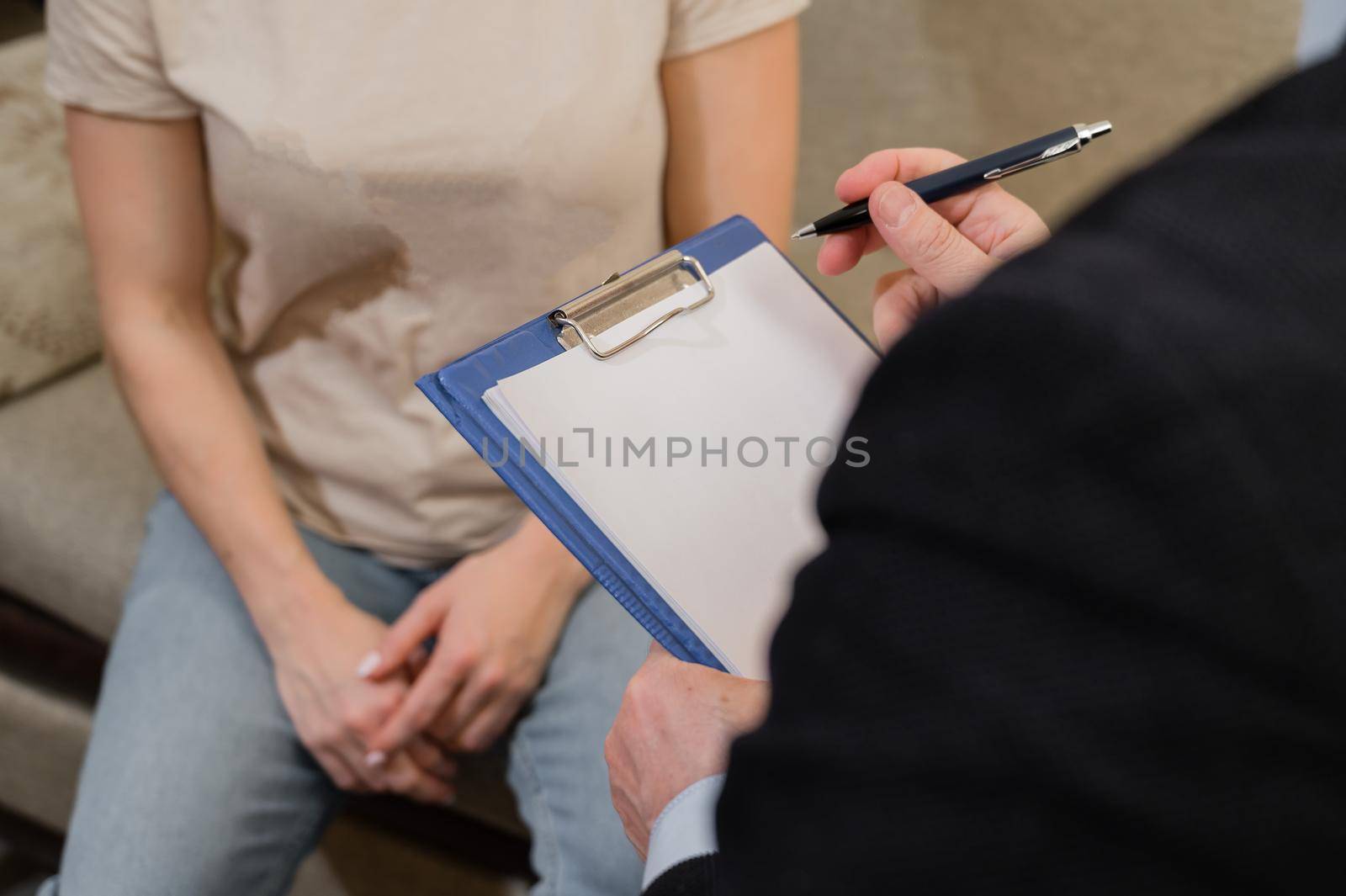 An elderly male psychotherapist talking to a female patient and taking notes on a clipboard. Close-up of the hands of a male psychologist.