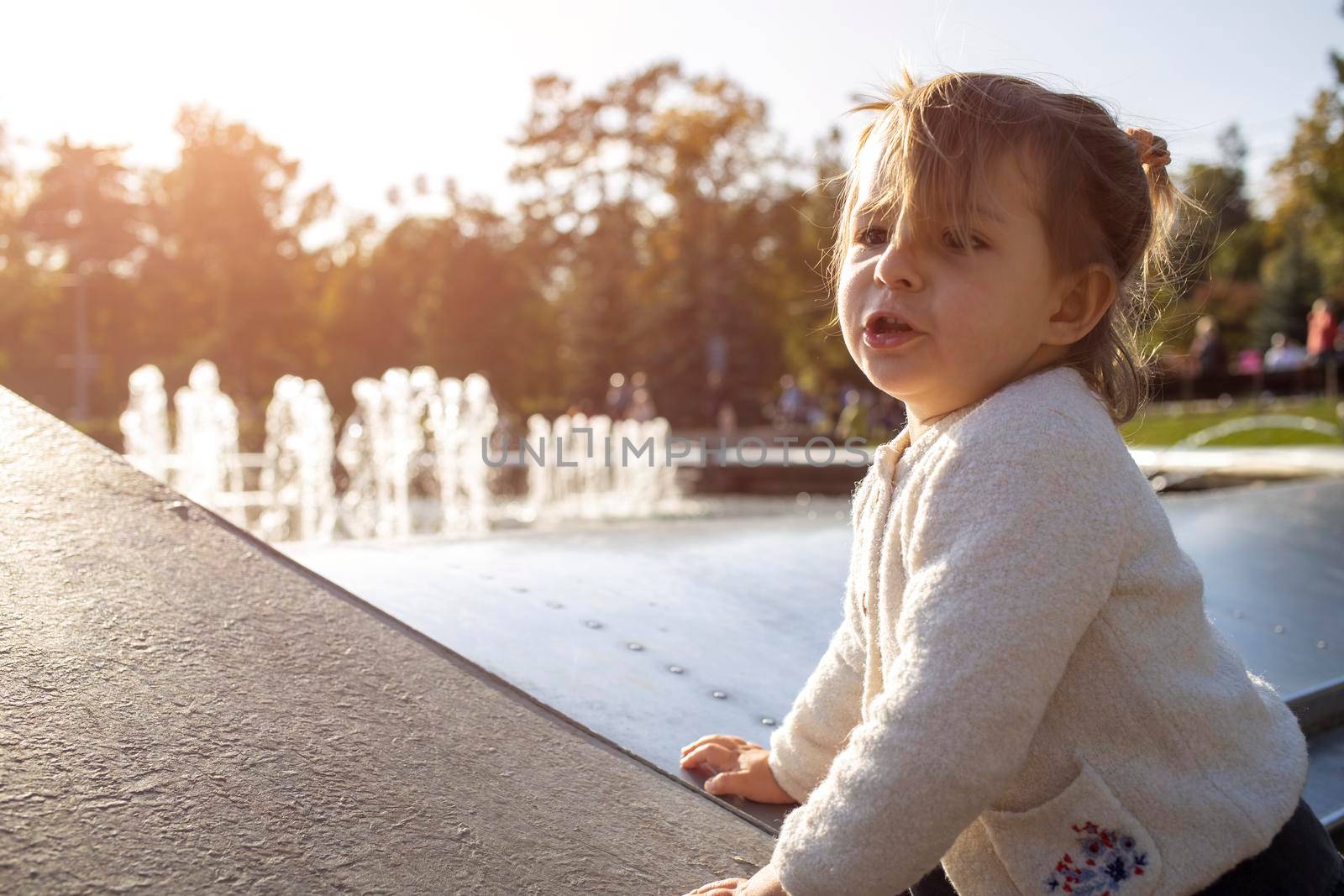 adorable toddler girl makes faces and grimaces against the backdrop of the park. the child plays cheerfully. happy childhood