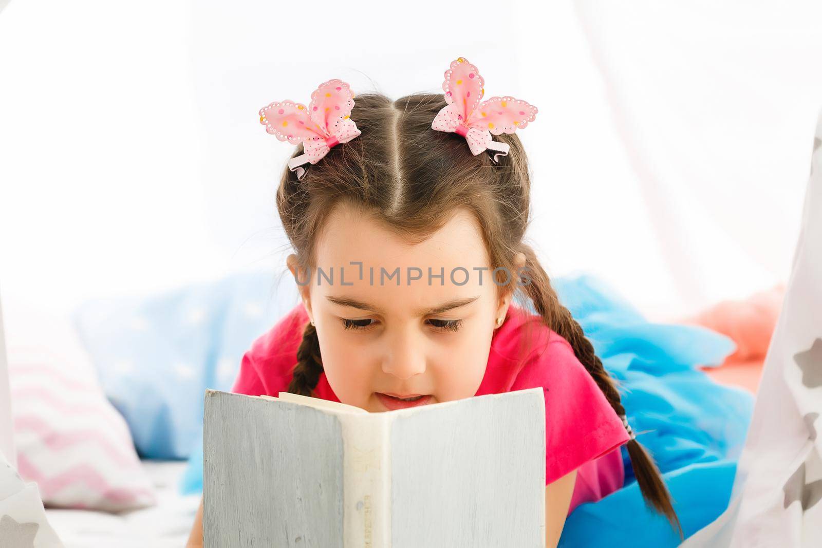 Enjoying great story. Cute little girl reading book while sitting on the floor in tent by Andelov13