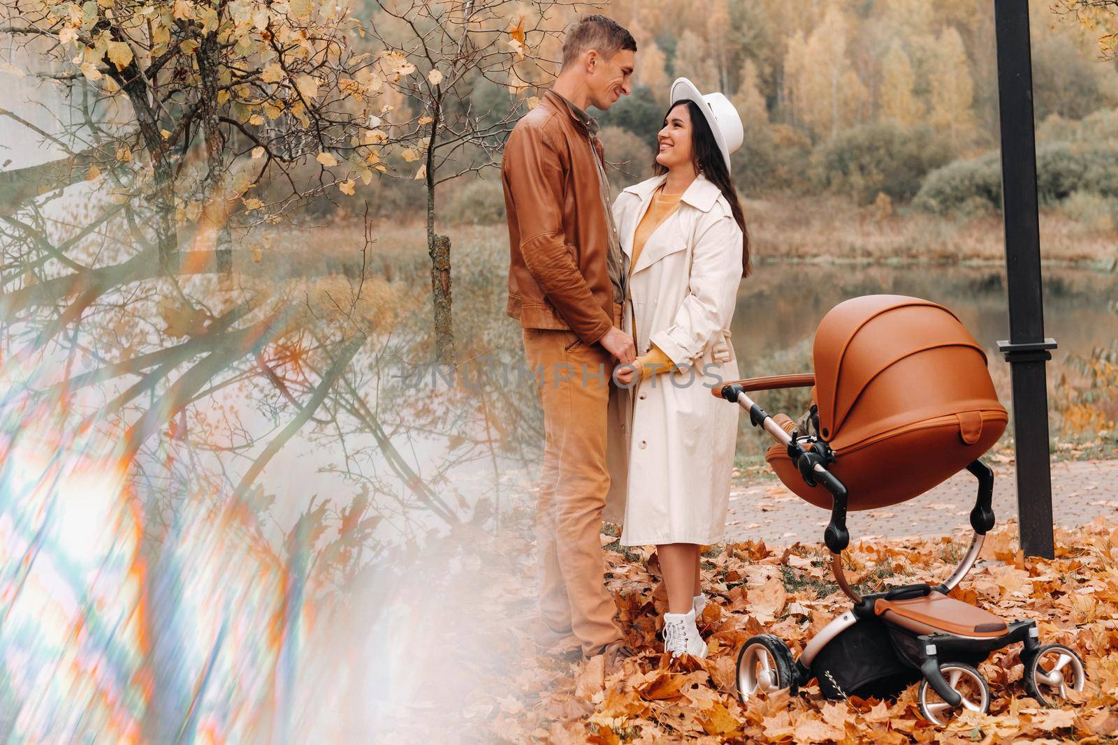 Father and mother on a walk with a stroller in the autumn Park. The family walks through the nature Park in the Golden autumn. by Lobachad