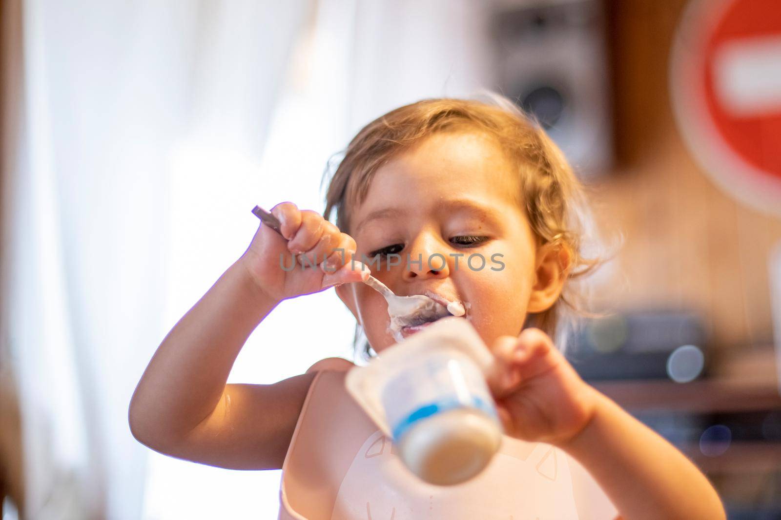 cute baby eating yogurt with spoon by himself. adorable toddler has lunch. hungry child eas food