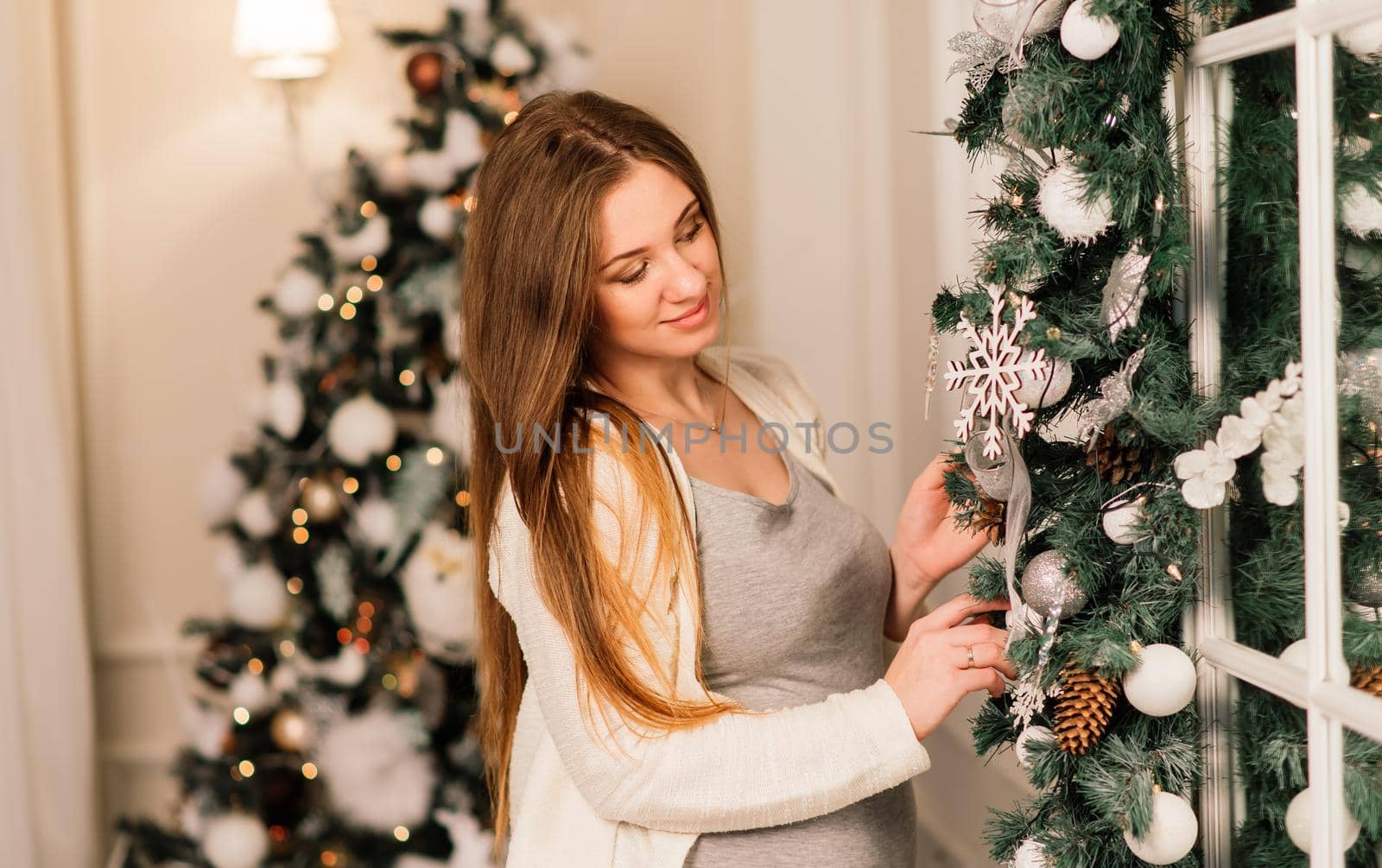 Close up of happy smiling pregnant woman touching her belly over christmas tree background by Zelenin
