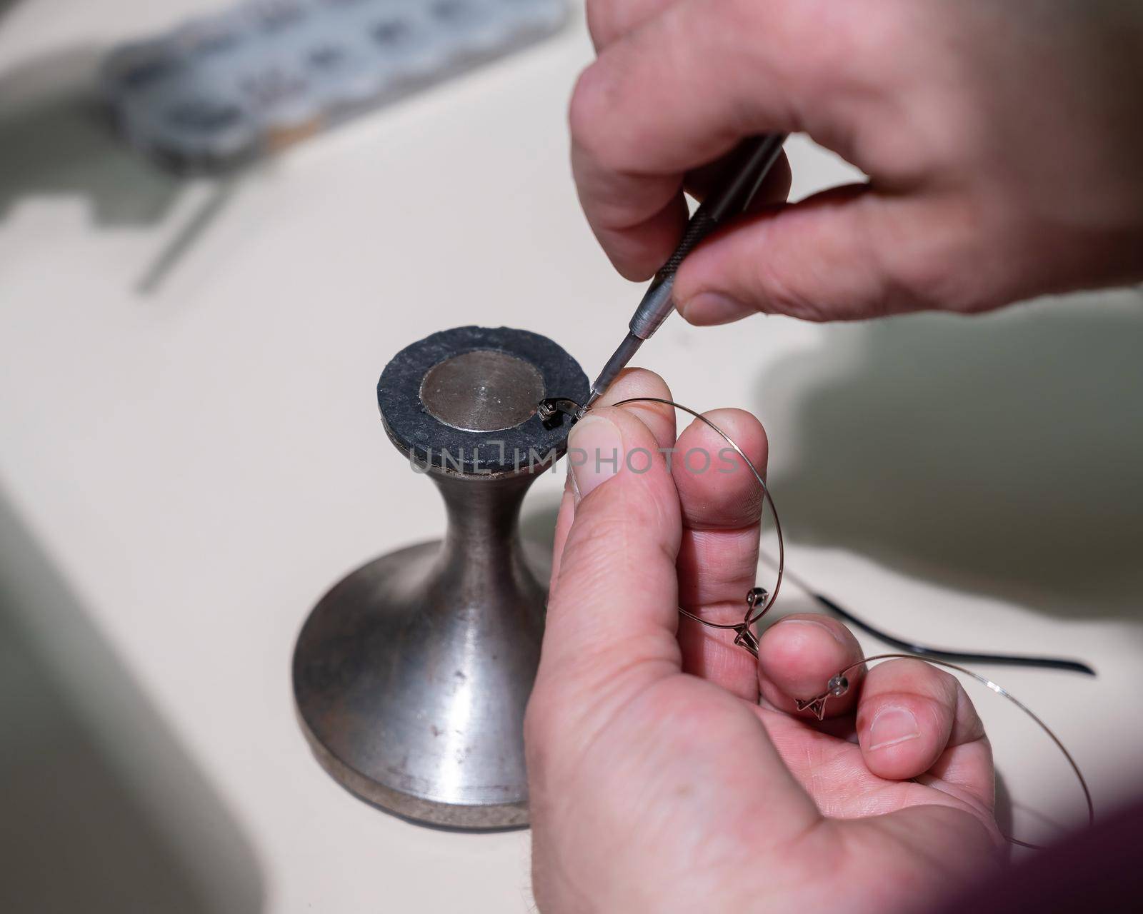 Optical technician fixing glasses. Close-up of male hands with screwdriver and goggles frame