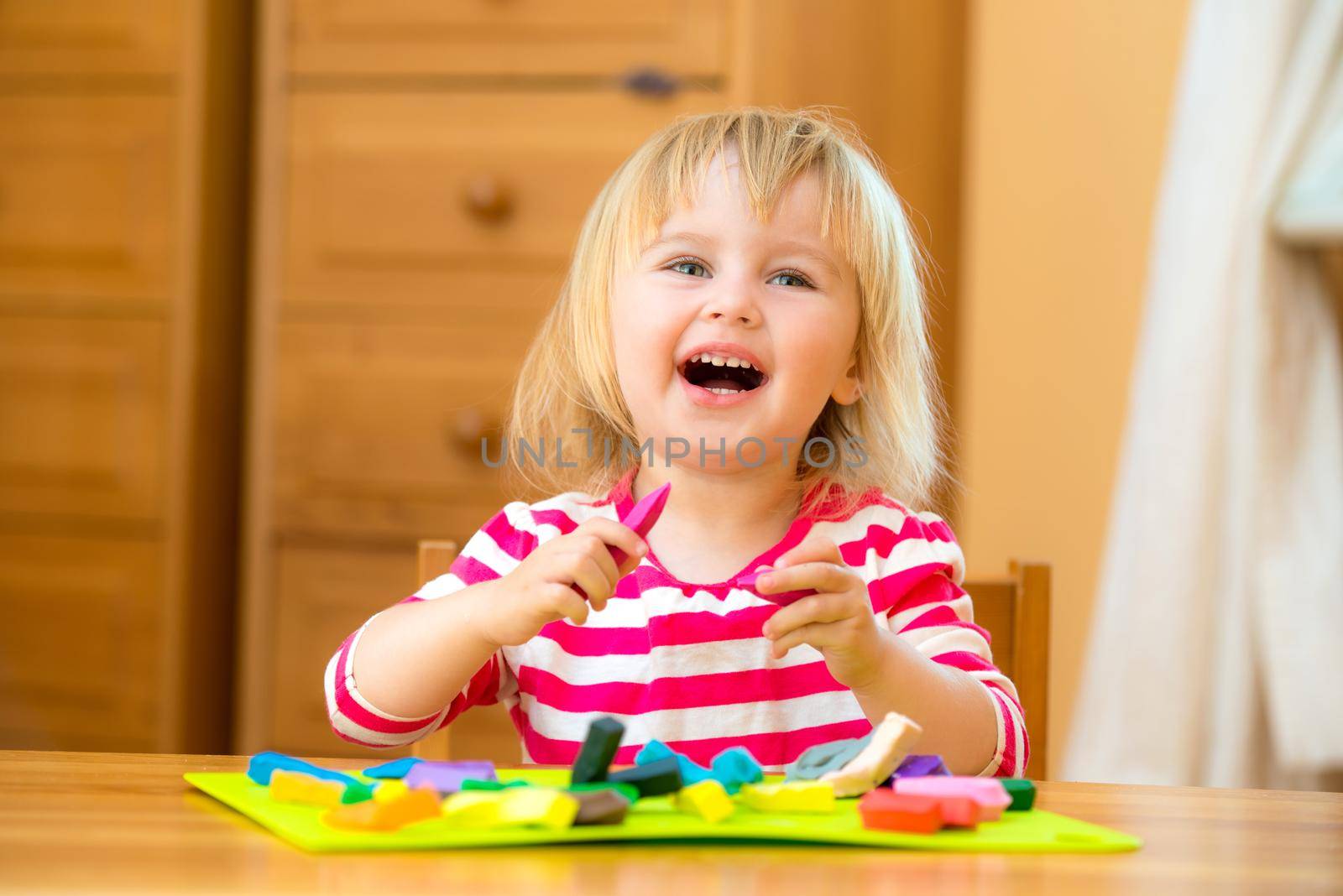 laughing llittle girl playing with plasticine at home