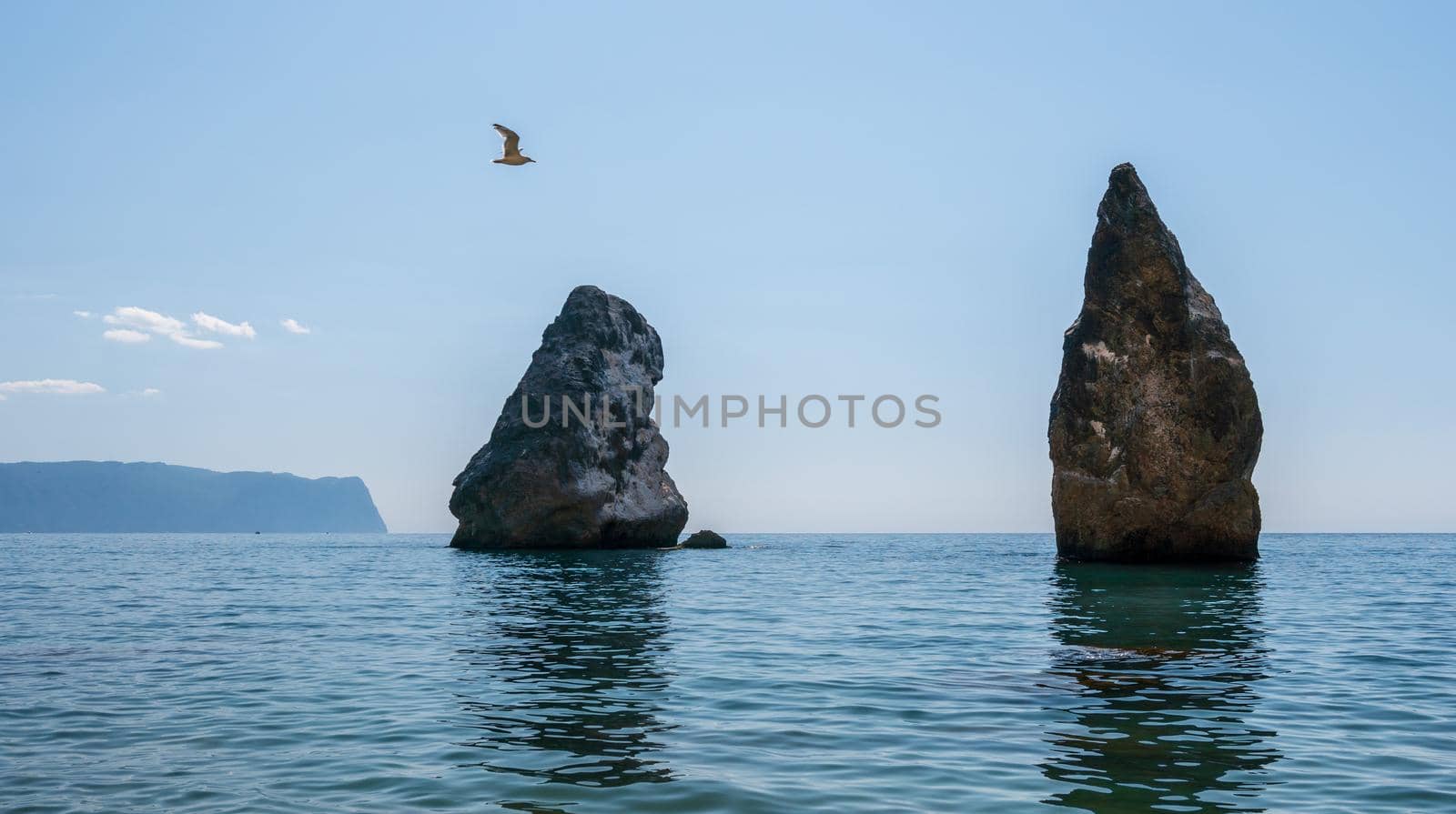 Summer sea landscape with clear sky and volcanic rocky coastline. Calm clear sea, small waves on the empty pebbles beach in rocky lagoon, volcanic basalt as in Iceland. Never-ending beauty of nature
