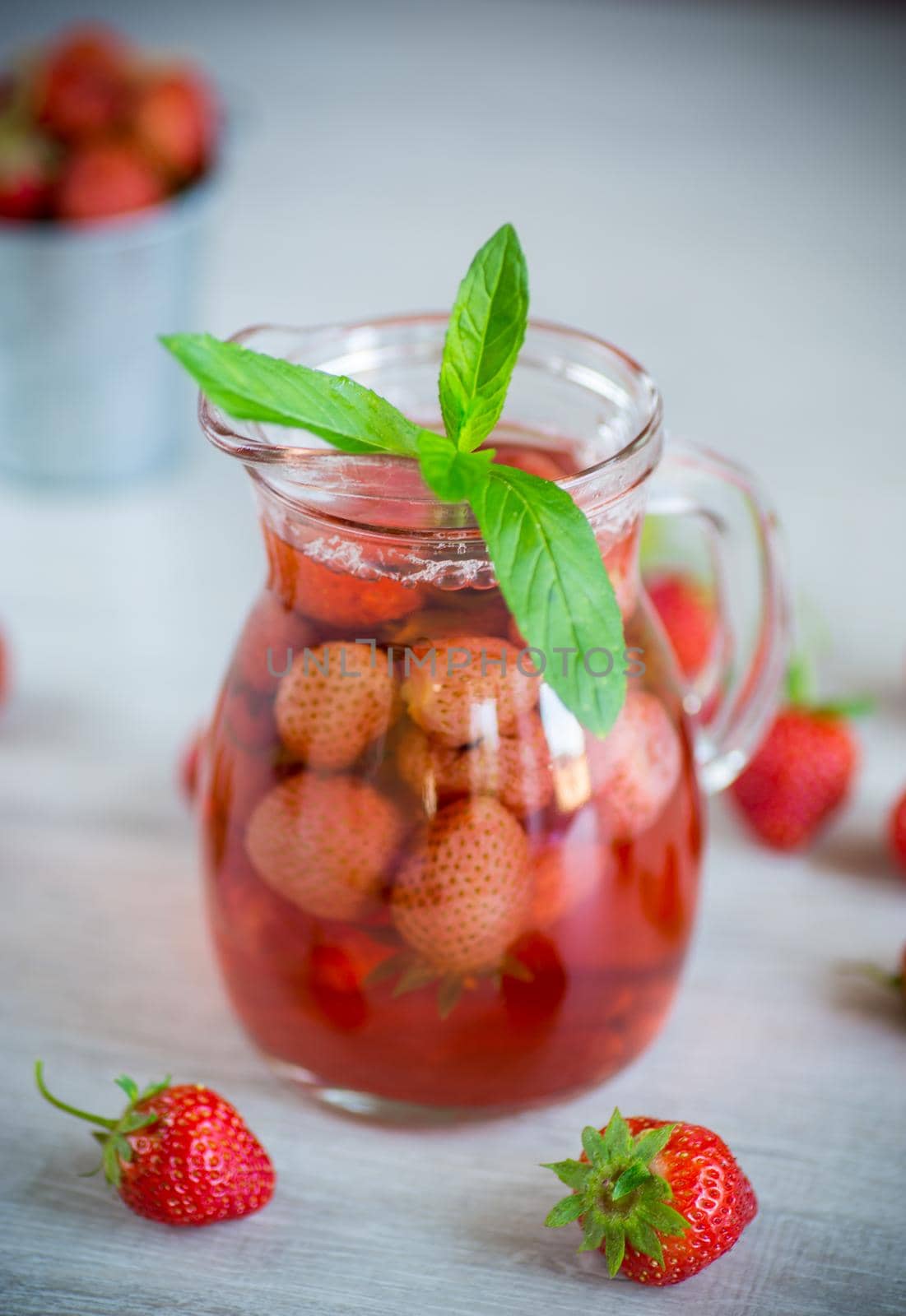 Sweet refreshing berry compote of ripe strawberries in a decanter on a wooden table