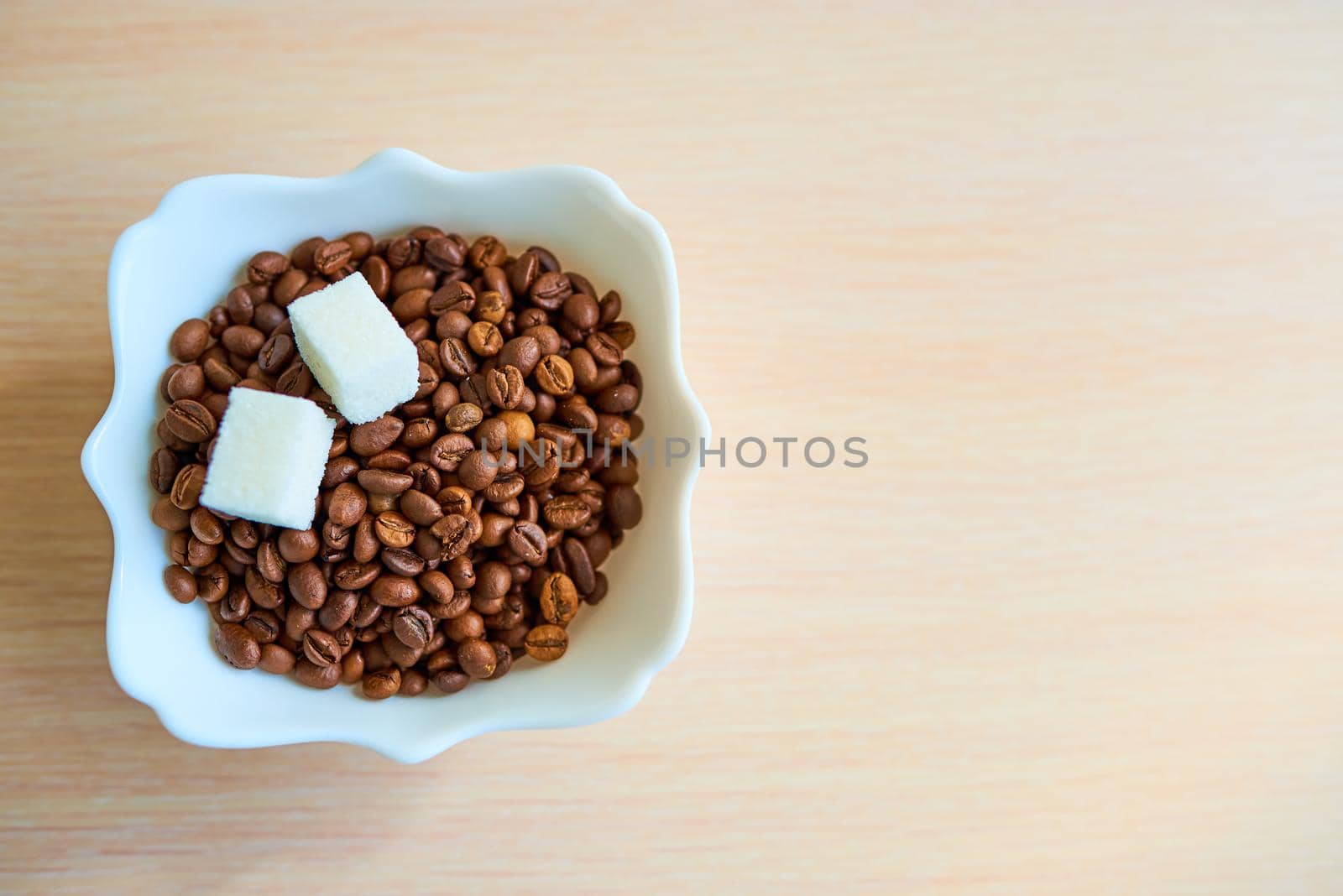 A plate with a bunch of coffee beans and two pieces of white sugar is on the table. Top view. Copy space. Assimilate concept.