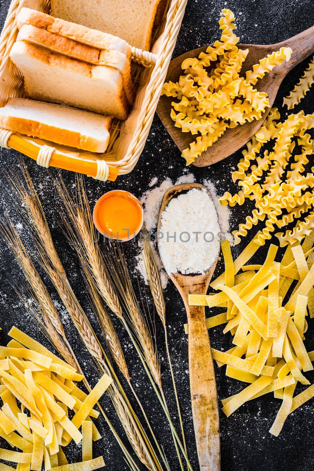 uncooked pasta, bread and other products on a black textured table