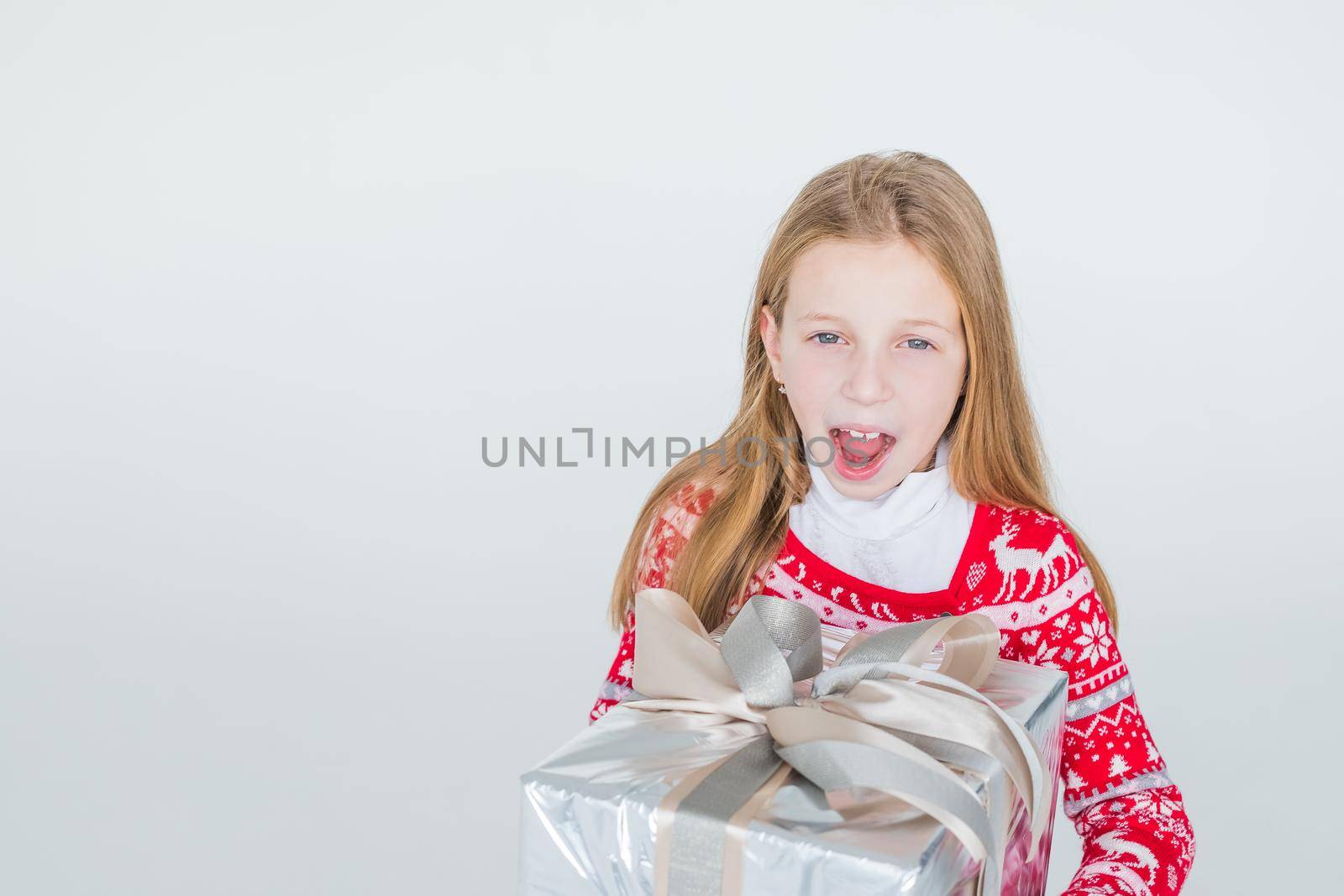 Joyous girl holding gift-wrapped box being excited and surprised to get present on white background.holidays, present, christmas, childhood, happiness concept.Excited surprised young girl in red dress by YuliaYaspe1979
