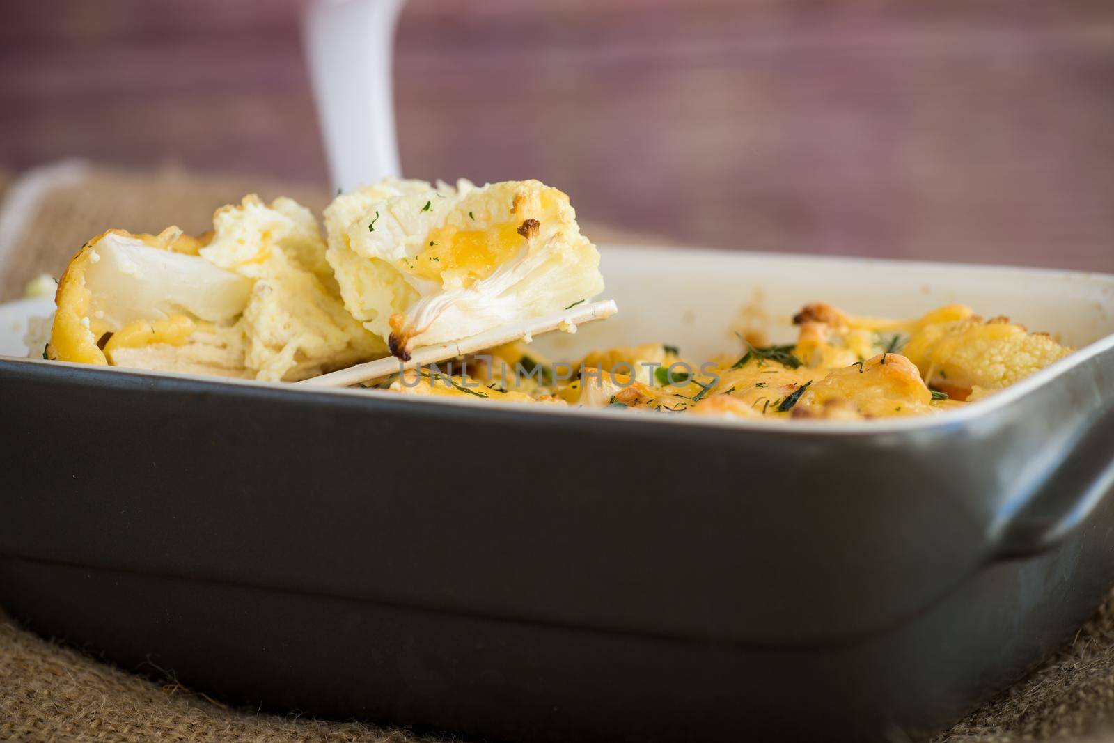 baked cauliflower with chicken fillet and vegetables topped with cheese in a ceramic mold