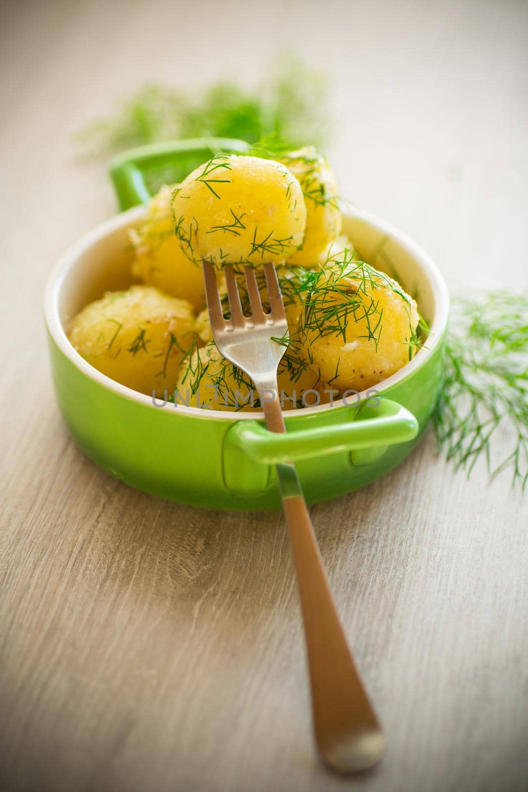 boiled early potatoes with butter and fresh dill in a bowl on a wooden table