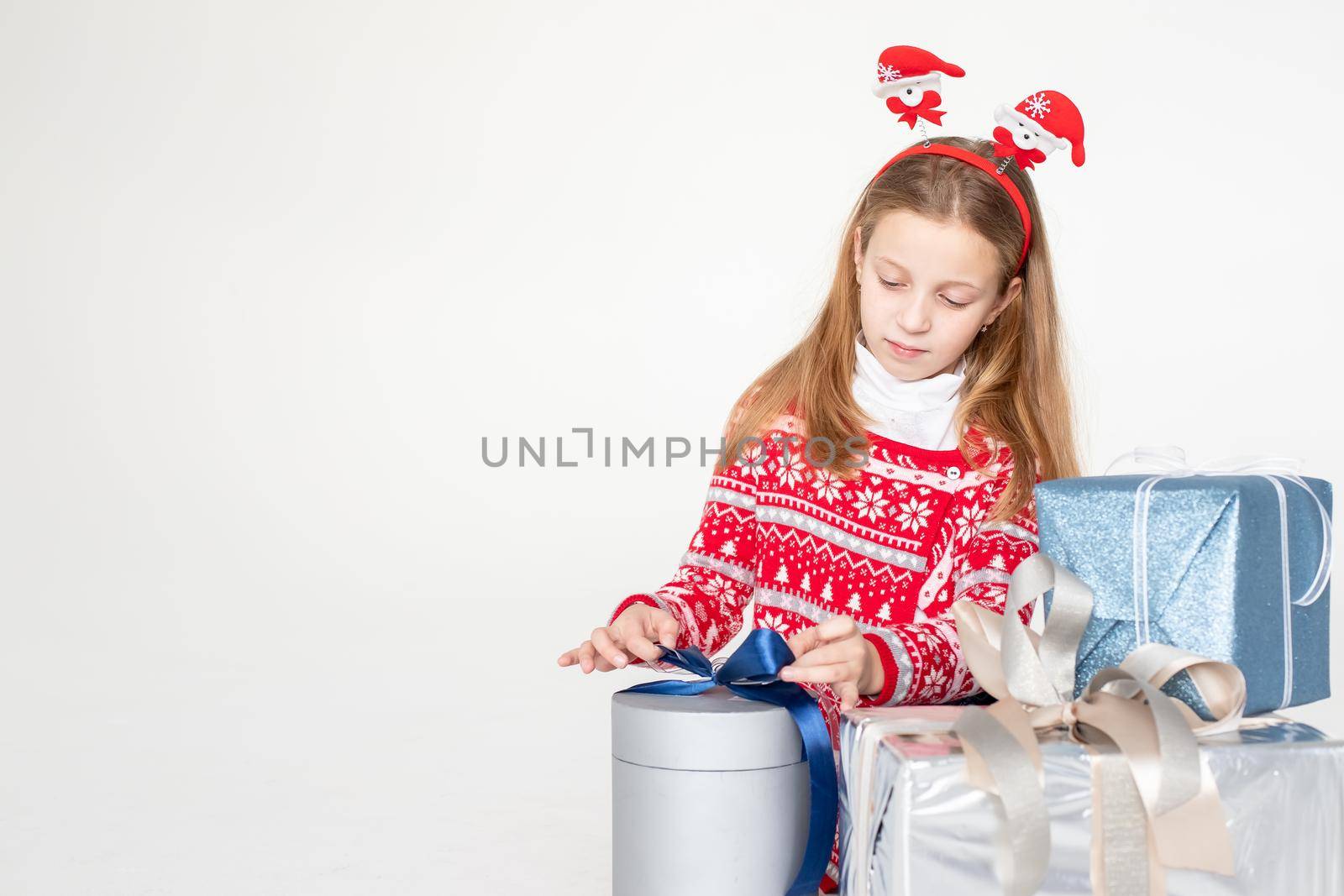 Pretty little girl wearing Christmas deer horns sitting isolated , holding stack of present boxes