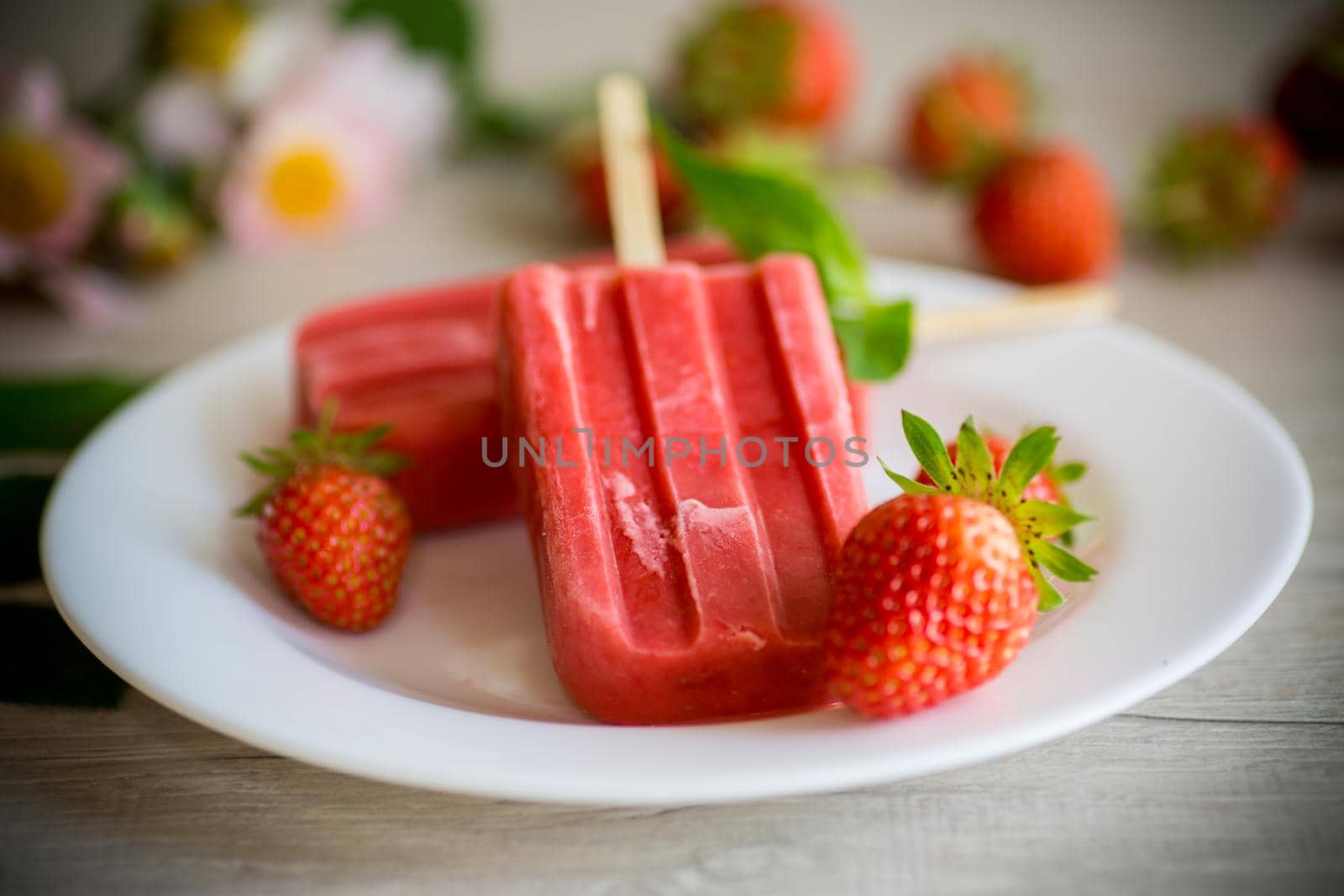 homemade strawberry ice cream on a stick made from fresh strawberries in a plate on a wooden table