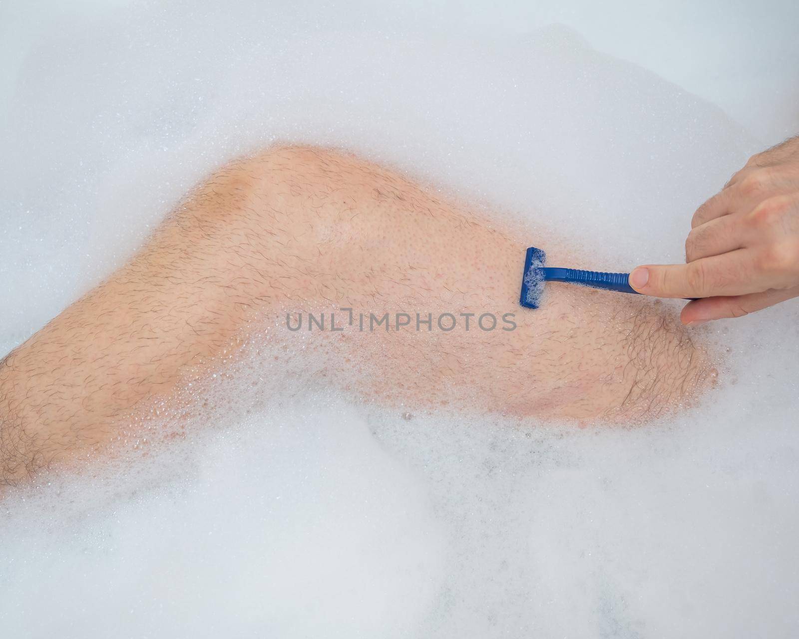 Funny picture of a man taking a relaxing bath and shaving his legs. Close-up of male feet in a bubble bath. Top view