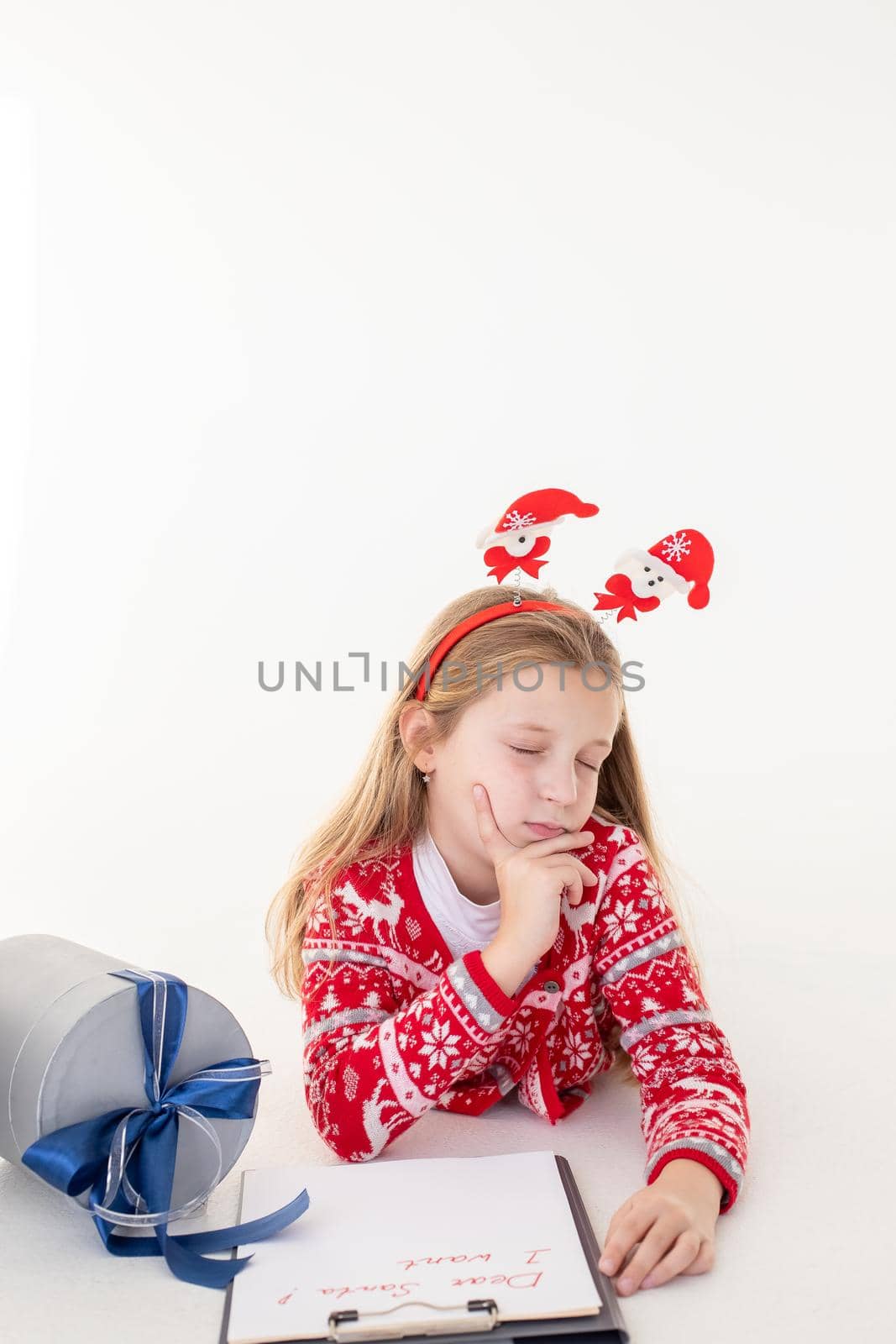 Thoughtful little girl writes letter to Santa Claus on white background.Goals plans dreams make to do list for new year christmas concept. Special orders for Santa. girl lying near the presents by YuliaYaspe1979