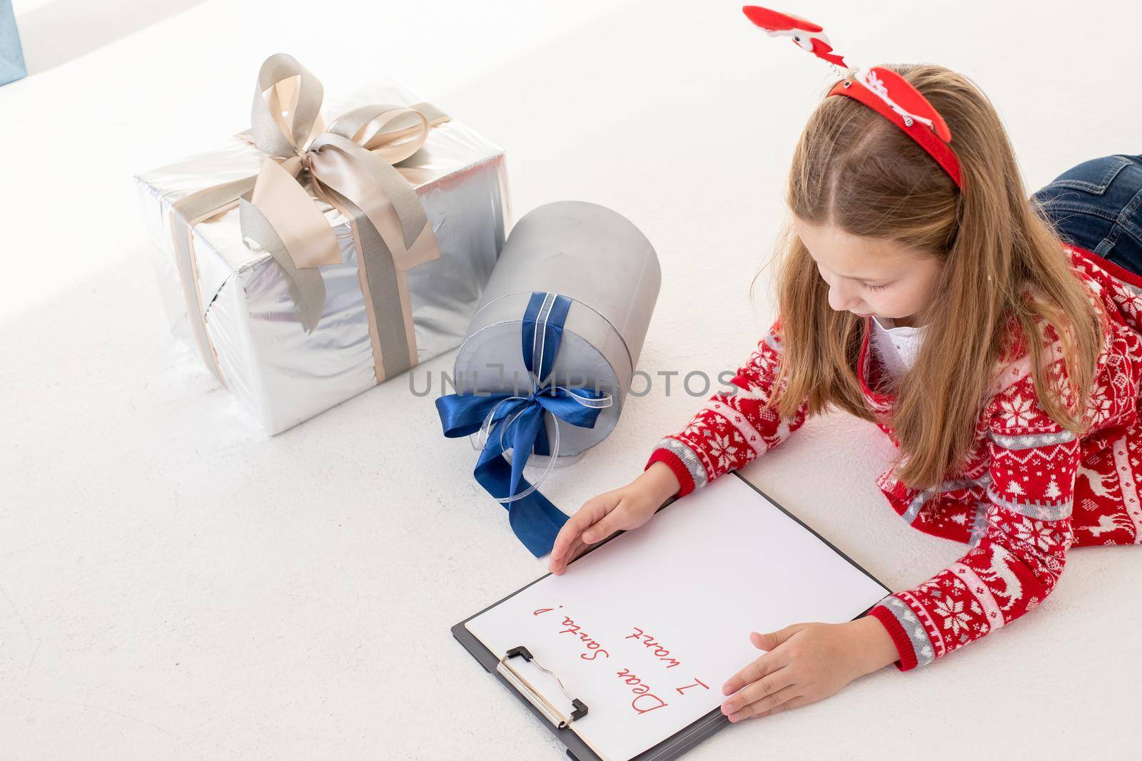 dear santa letter written by a child for Christmas.Concentrated kid is involved in the process of thinking over all her wishes and desires. Pretty Girl hold clipboard and paper near gift box. by YuliaYaspe1979