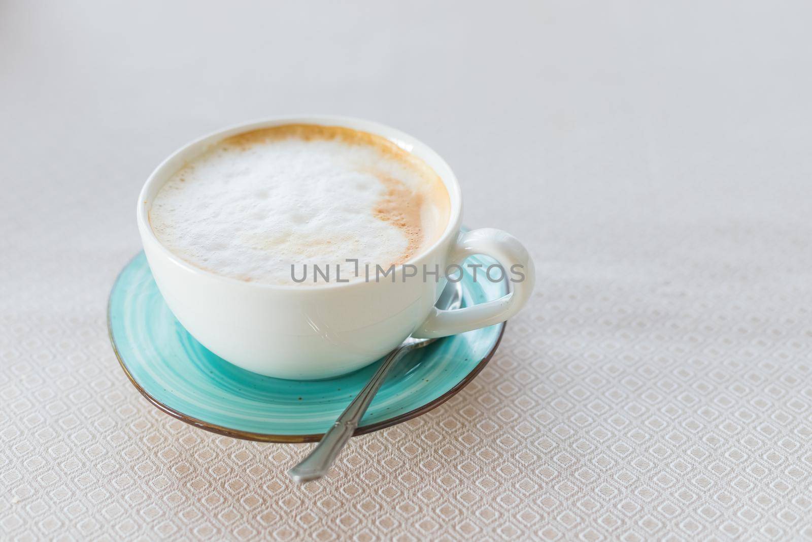 Hot coffee cappuccino latte art in jade color cup isolated on beige table.Cappuccino coffee cup top view.Latte art on milky foam.Hot Italian energizing beverage served in green ceramic mug by YuliaYaspe1979