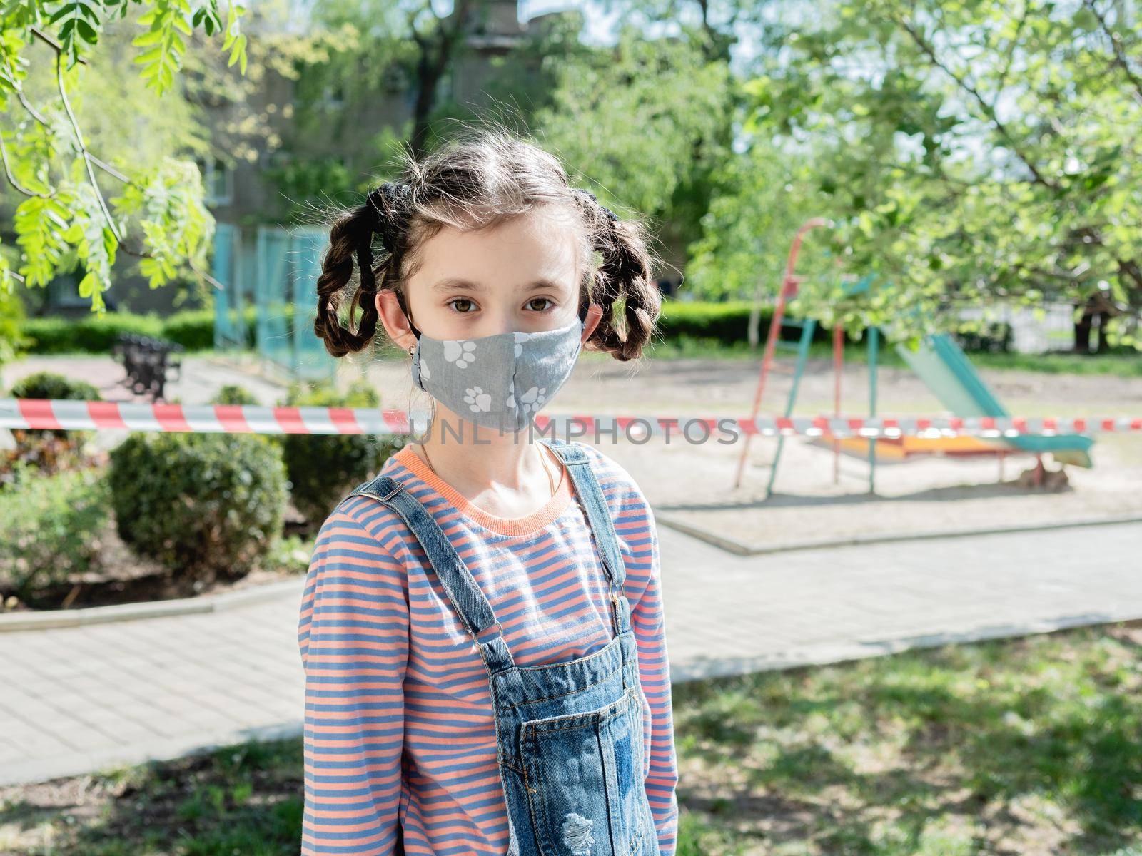 A little girl in a medical mask is not allowed to play in the playground during the coronavirus pandemic.