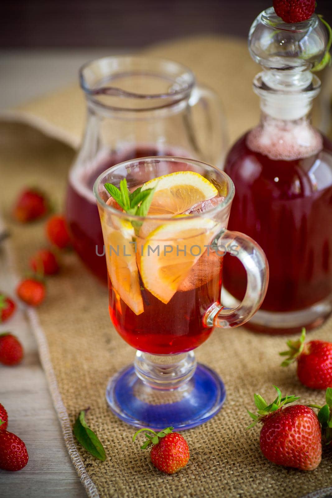 refreshing cool strawberry lemonade with lemon, ice and mint in a glass on a wooden table