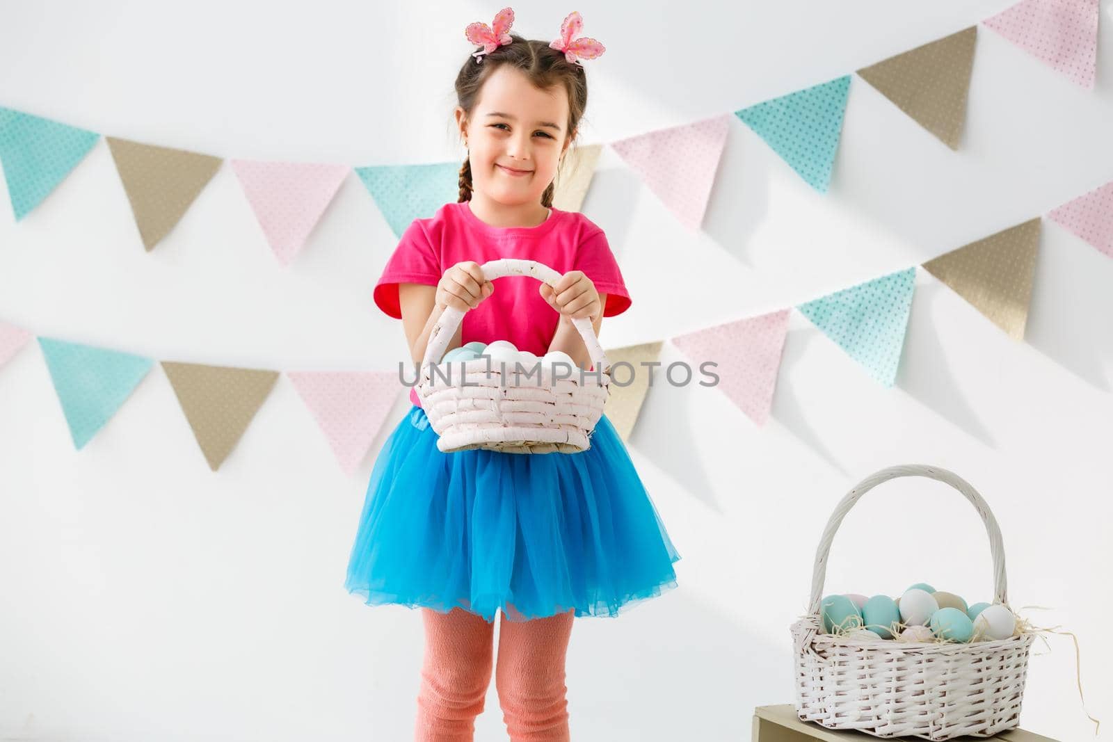 Getting ready to Easter. Lovely little girl holding an Easter egg and smiling with decoration in the background