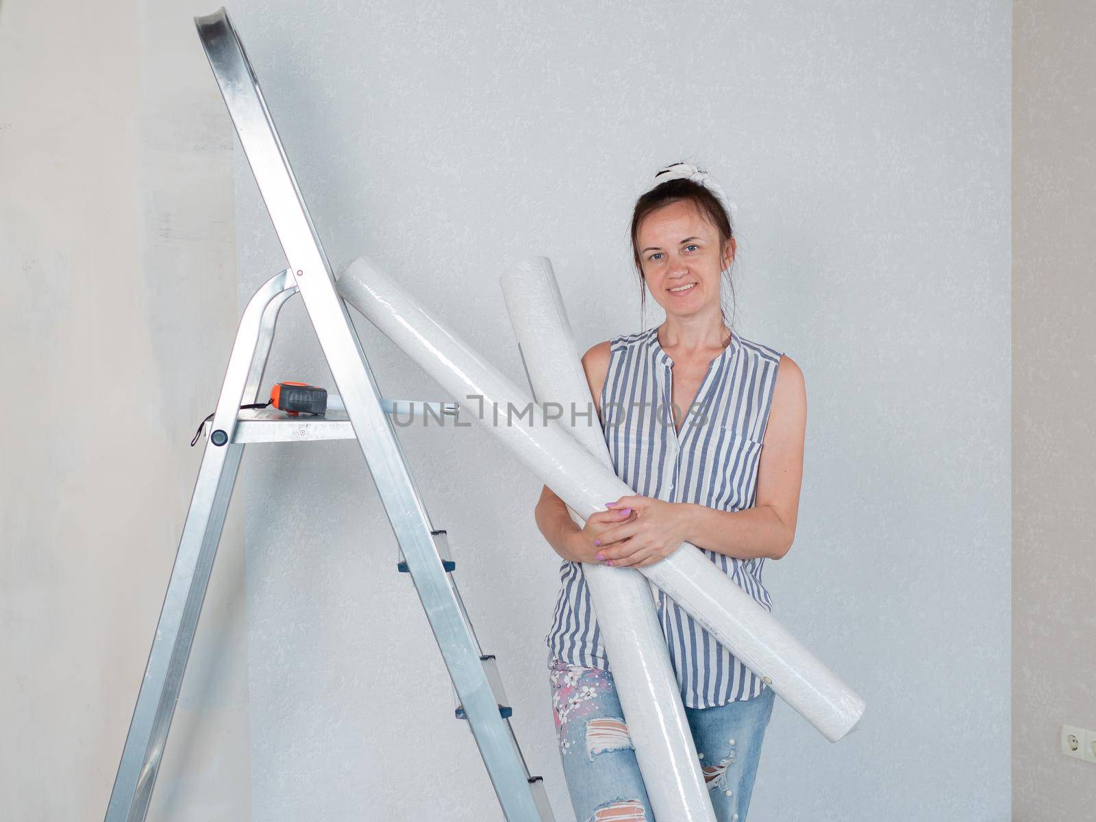 A woman with rolls of Wallpaper in the room smiles. Repairs in the apartment. Wallpapering in the room.