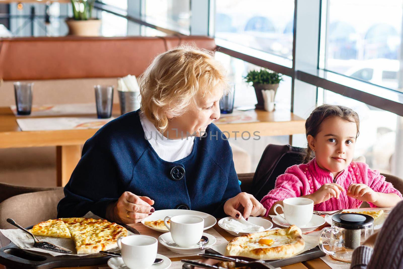 childhood and people concept - happy grandmother and little girl with spoon eating at outdoor cafe or restaurant