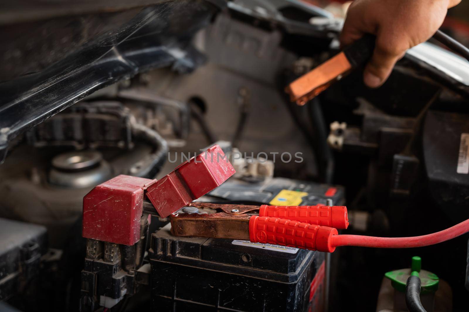 The mechanic connects the clamps to the discharged car battery