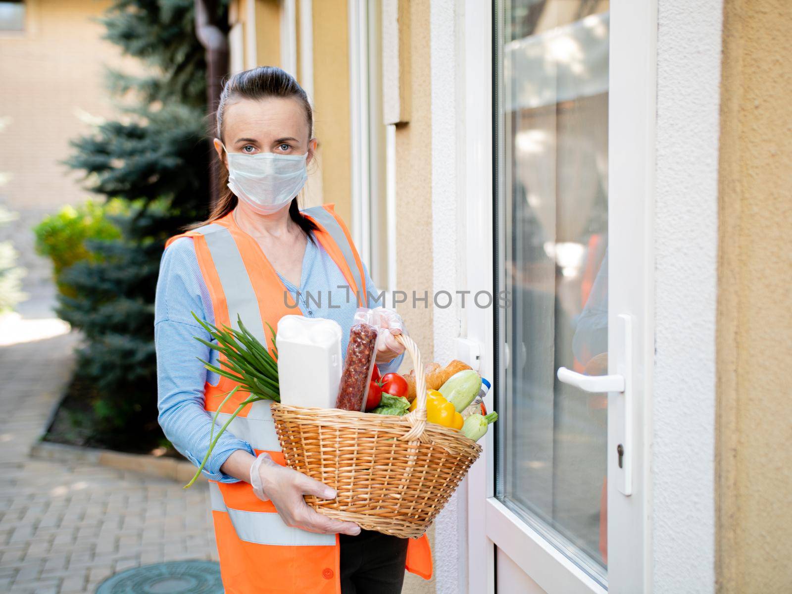 Portrait of a volunteer girl with a basket filled with food at the door of a person who is self-isolated during the coronavirus pandemic.