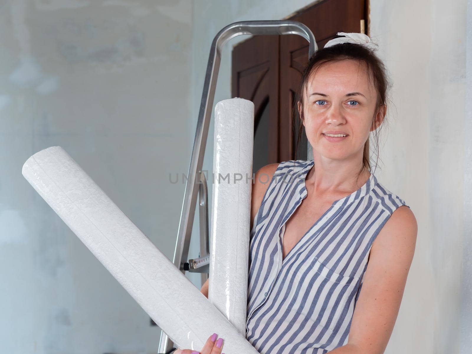 A happy woman holds rolls of new Wallpaper in her hands. Repairs in the apartment. Wallpapering.