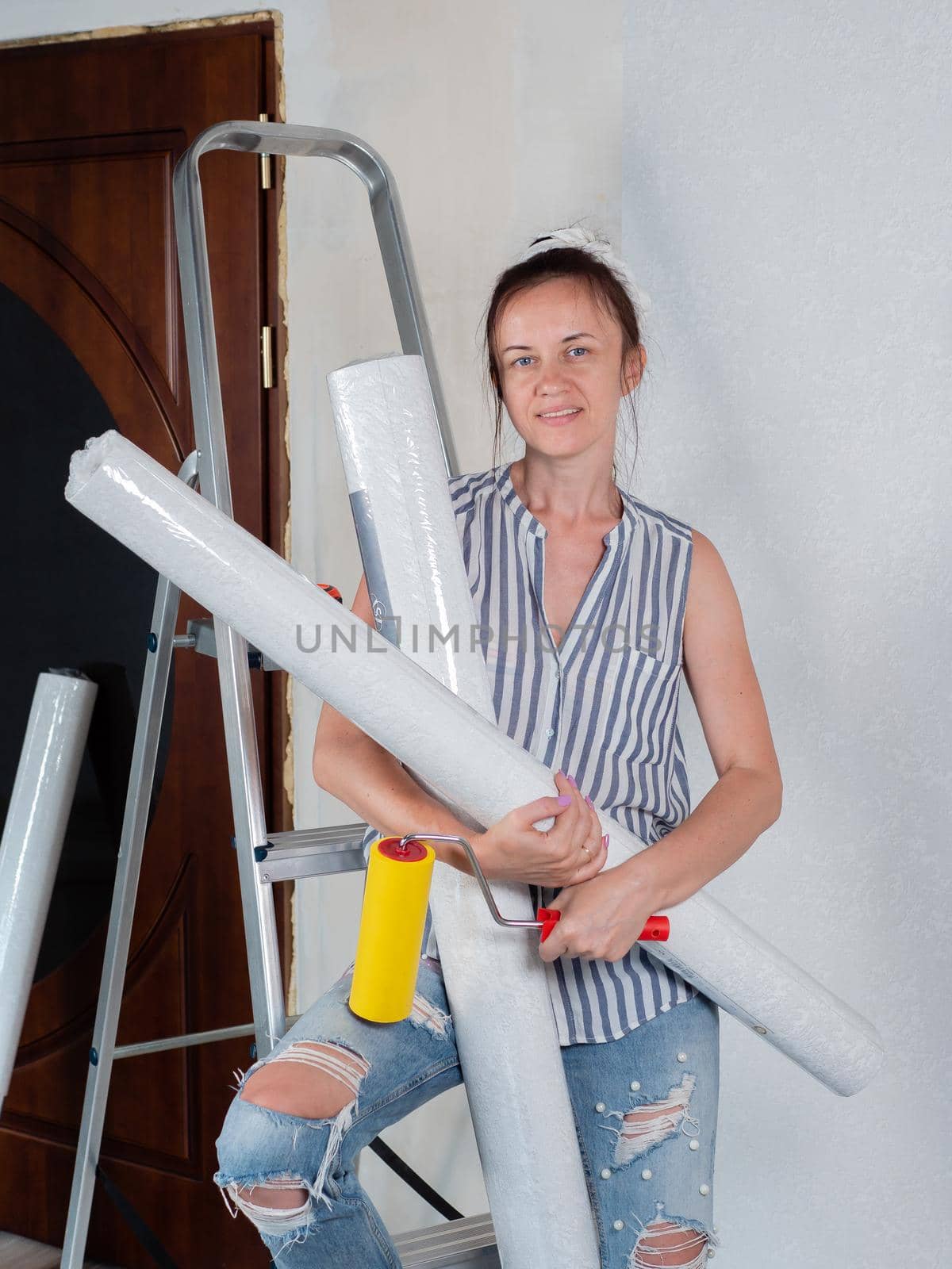 Repairs in the apartment. Wallpapering. Portrait of a woman with rolls of Wallpaper near the stepladder in the room. by Utlanov