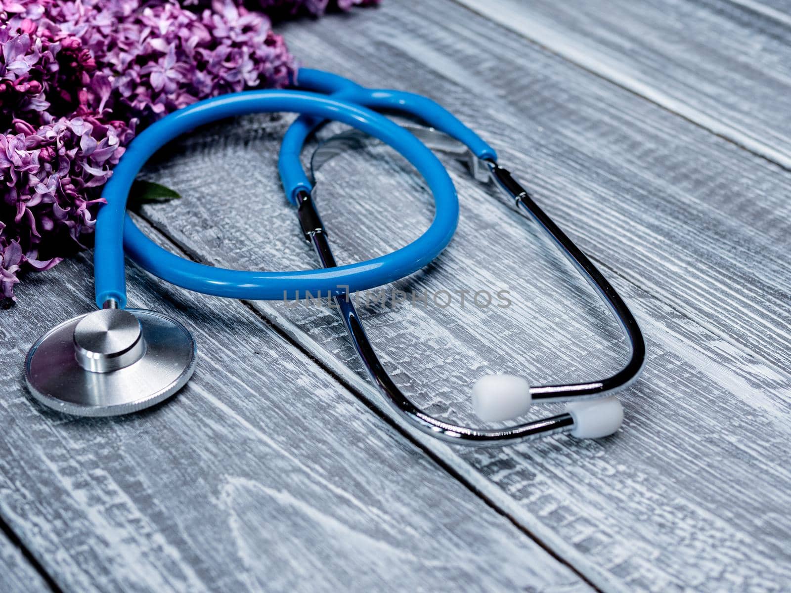 Stethoscope or phonendoscope on a wooden deck next to a bouquet of lilacs. Medical and healthcare concept.