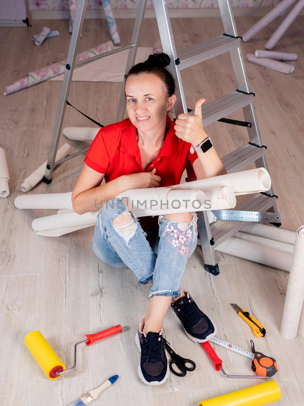 Portrait of a woman sitting on the floor with rolls of Wallpaper in her hands on the background of a stepladder. by Utlanov