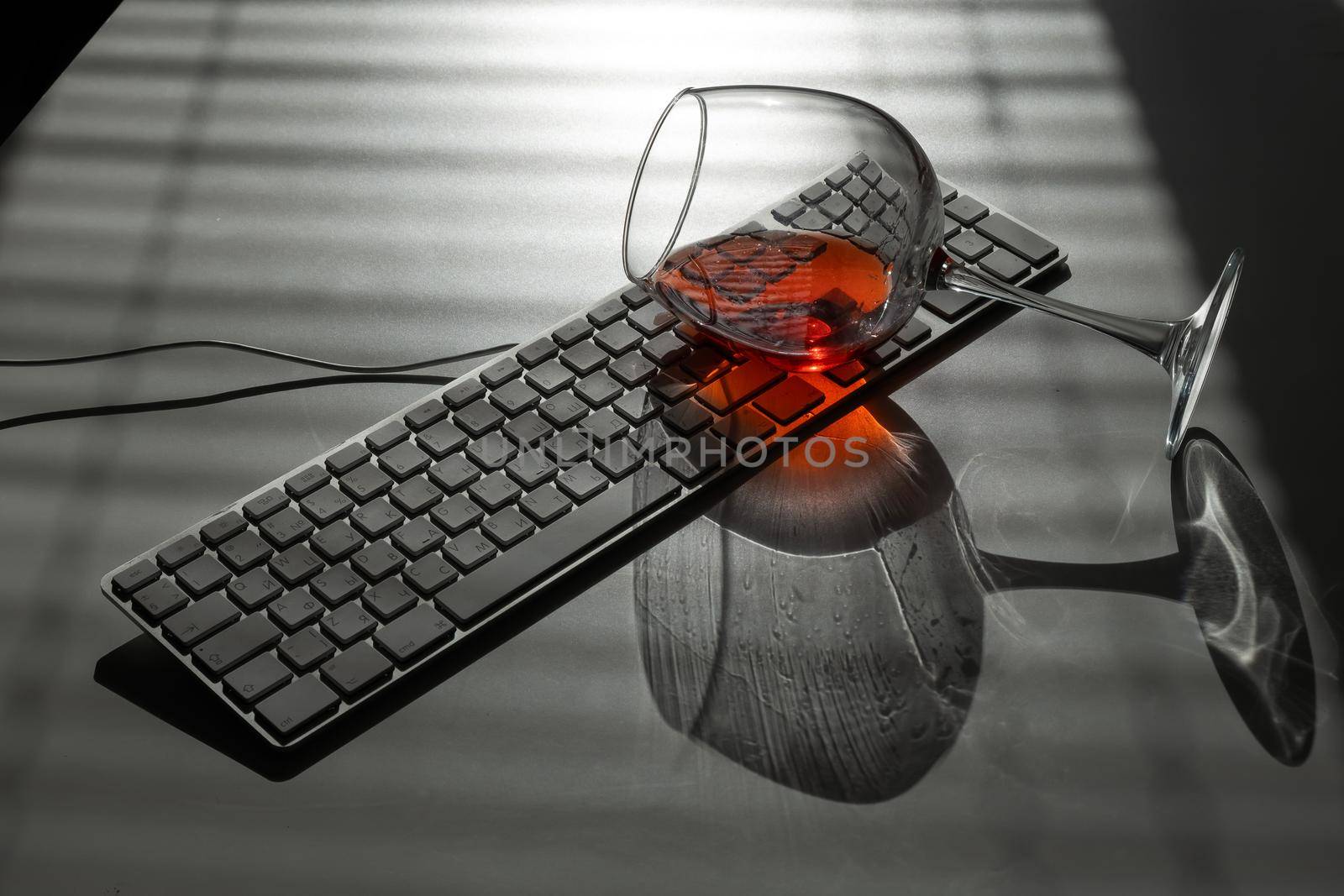 A glass of red wine lies on the keyboard on a white table with a shade from the blinds by mrwed54