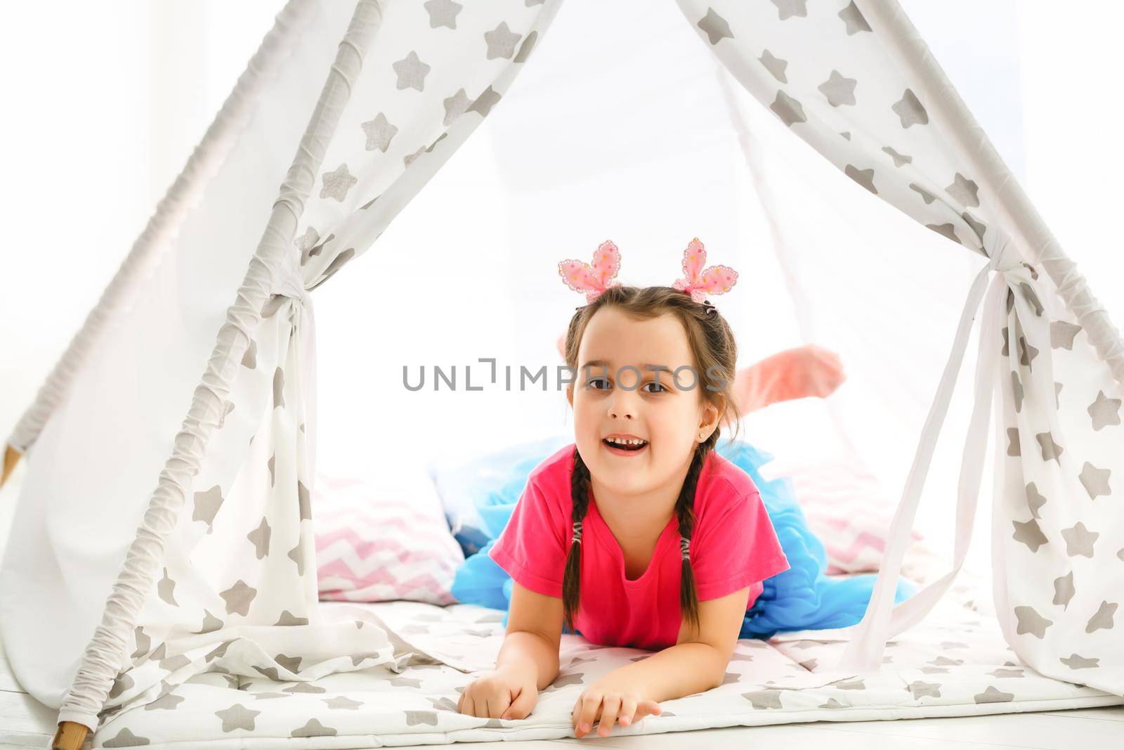 A little girl sits in a wigwam with pillows