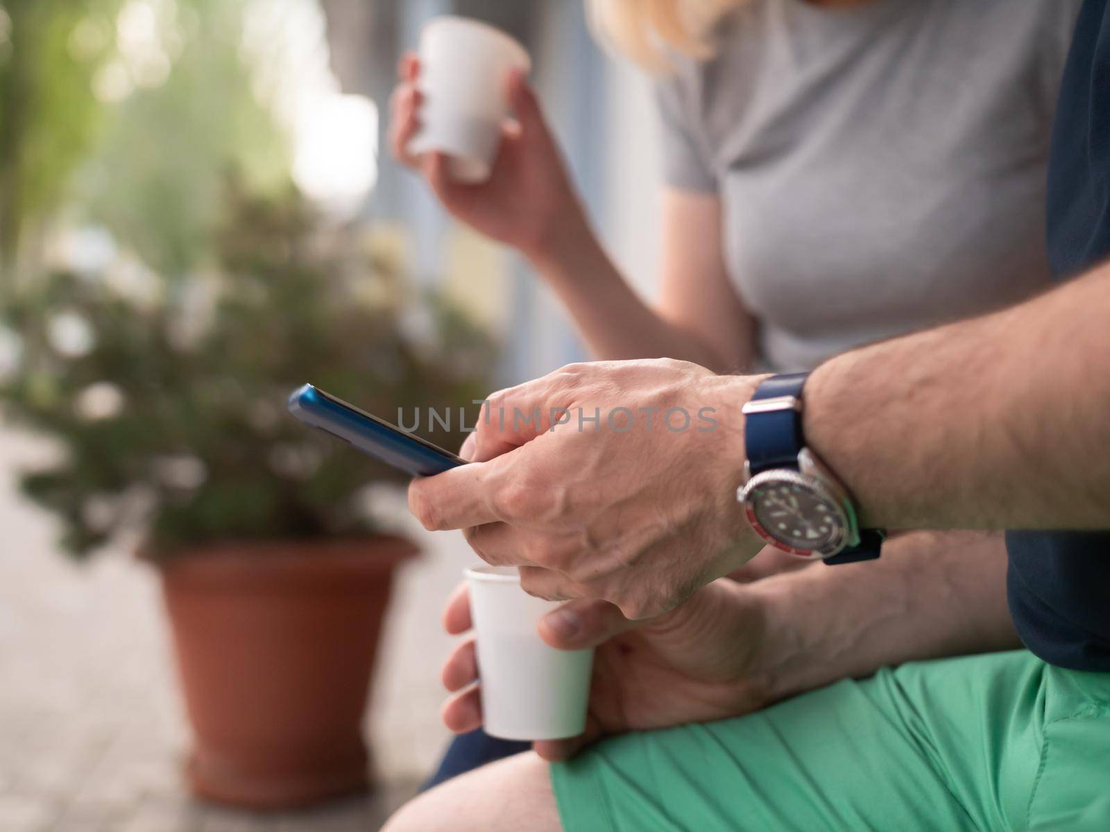 A couple of men and women look at the smartphone screen during a coffee break in a street restaurant. Close-up of male hands holding a smartphone.