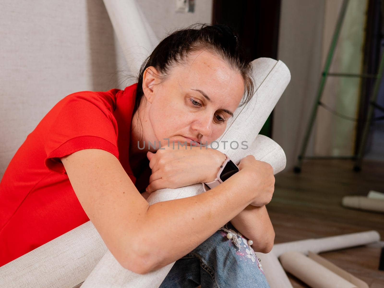 Portrait of a tired and sad woman sitting on the floor with rolls of Wallpaper in her hands. by Utlanov