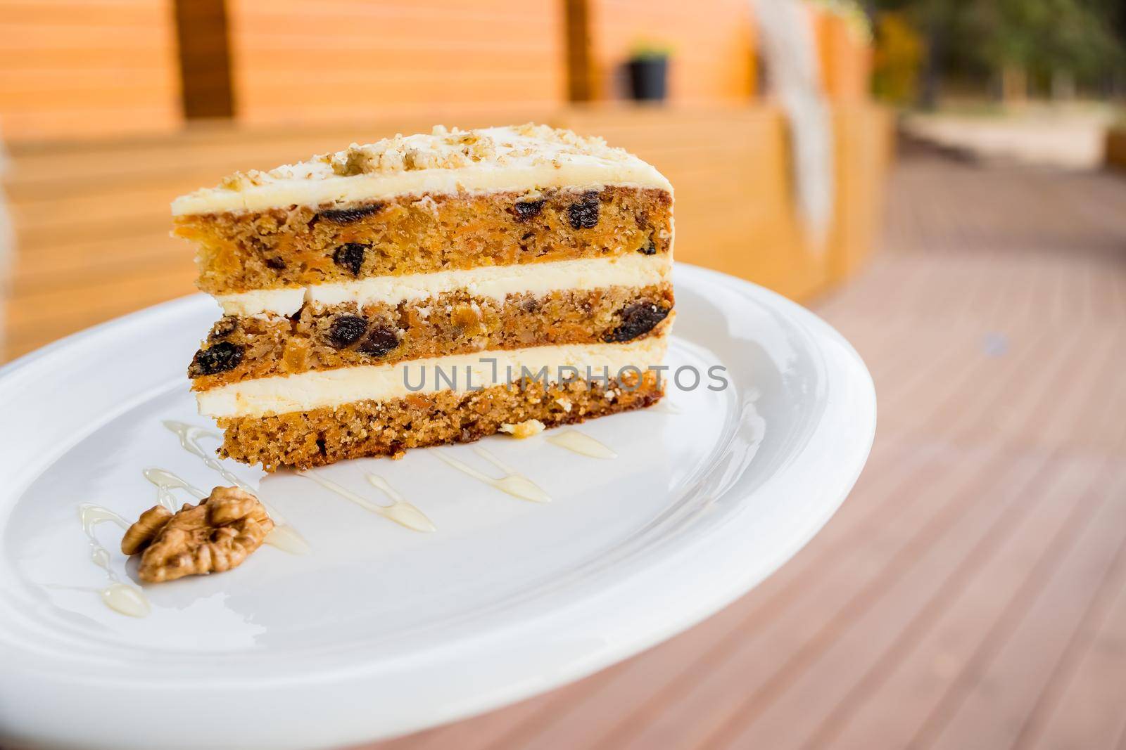 Close-up of walnut carrot cake on white plate with red background in soft focus.