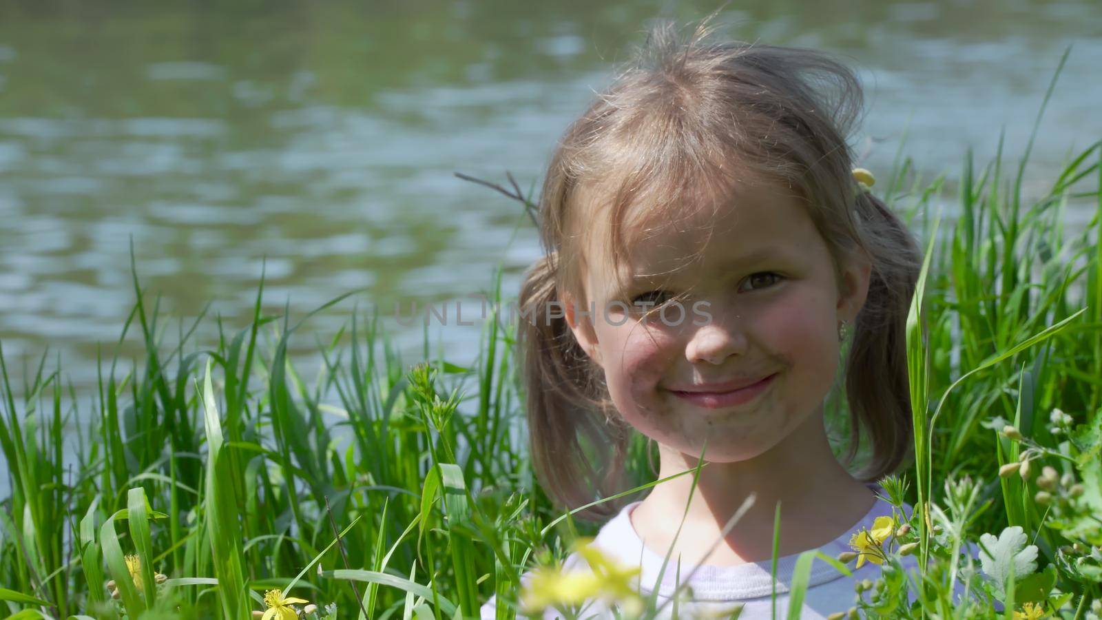 Portrait of a smiling little girl. Baby girl sitting in tall grass. Tiny kid have fun, enjoy nature outdoors.