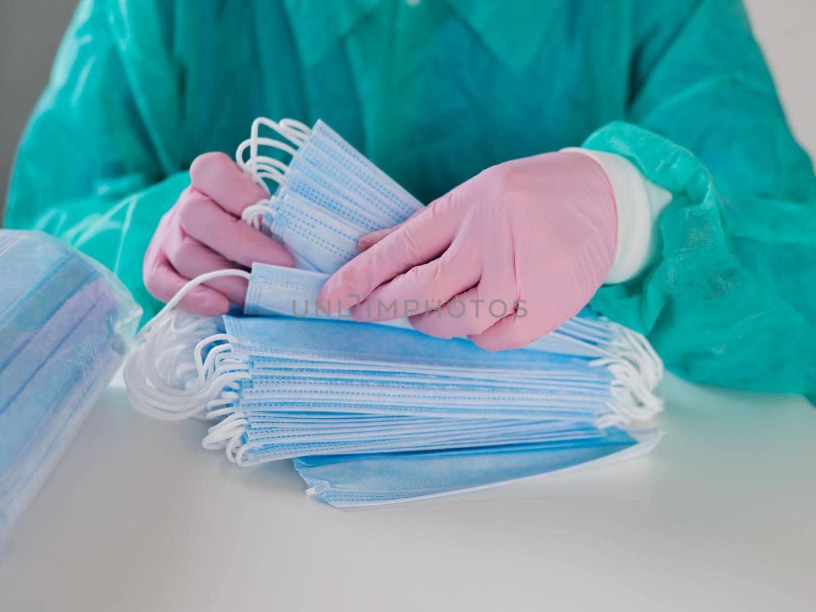 Close-up of a gloved woman counting blue masks at a table.