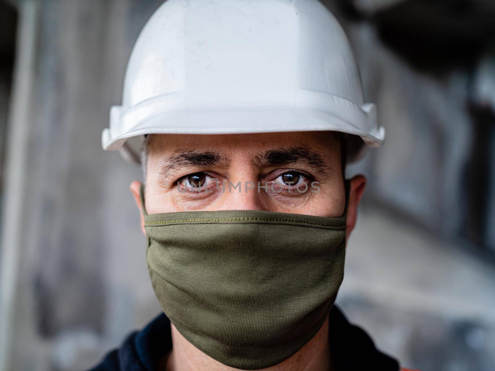 Portrait of foreman wearing mask and hardhat at construction site, building in background. Concept of coronavirus social distance and covid-19.