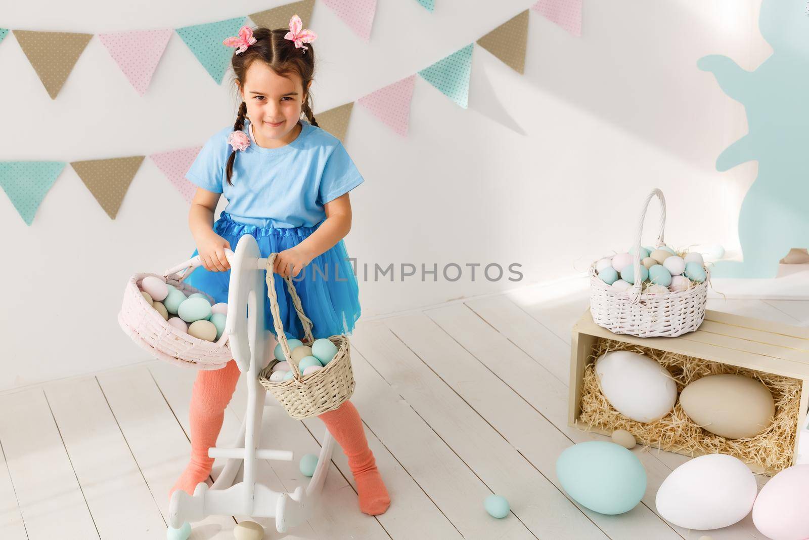 Getting ready to Easter. Lovely little girl holding an Easter egg and smiling with decoration in the background by Andelov13