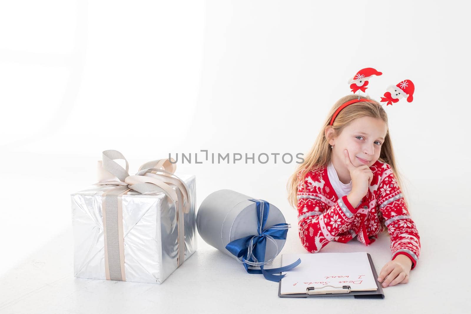 Thoughtful little girl writes letter to Santa Claus on white background.Goals plans dreams make to do list for new year christmas concept. Special orders for Santa. girl lying near the presents by YuliaYaspe1979